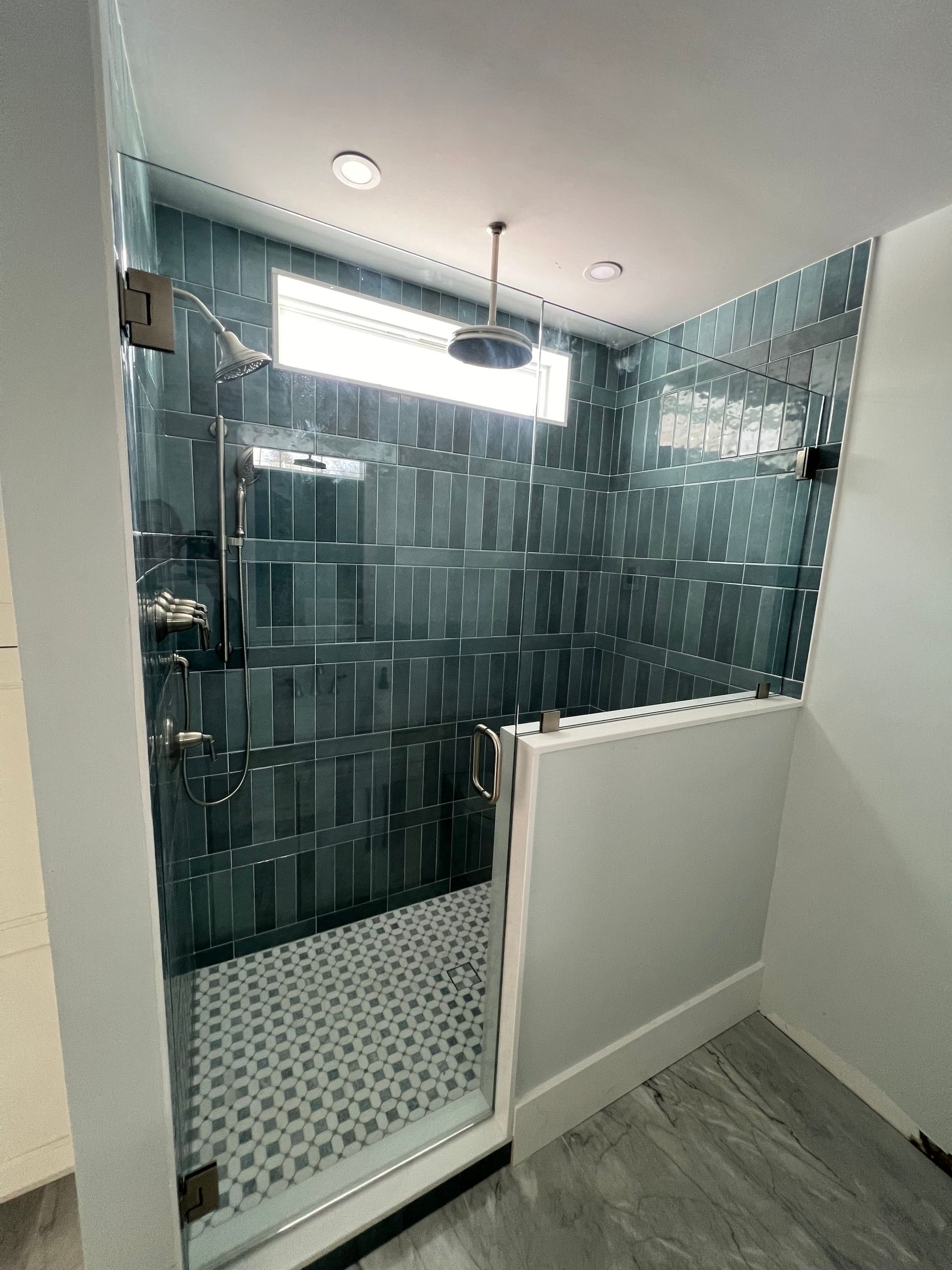 Modern shower with teal tile, glass door, rain shower head, and patterned floor.