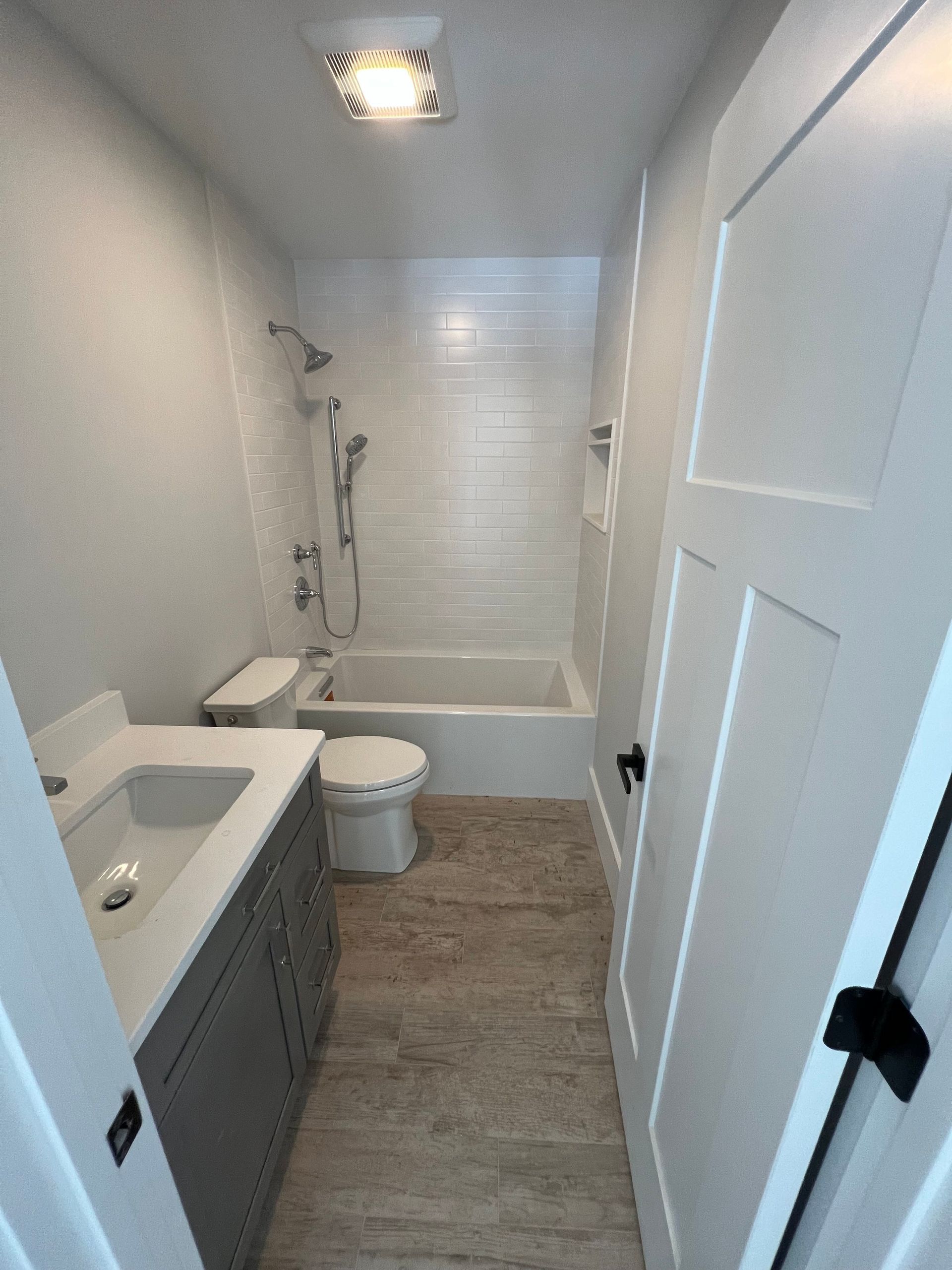 Small, narrow bathroom with a white tub, toilet, and vanity with a gray cabinet.