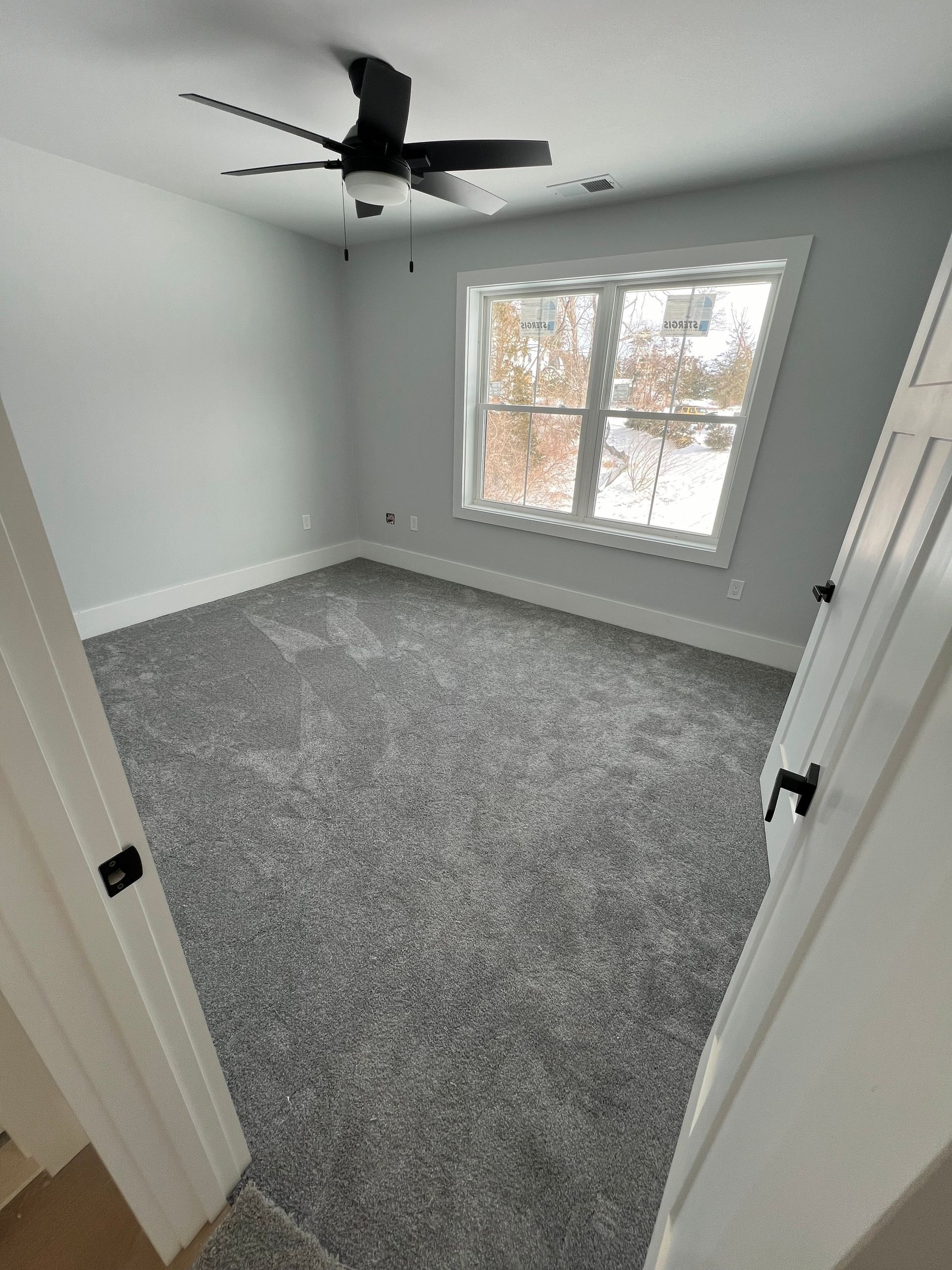 Empty room with gray carpet, light blue walls, a window, and ceiling fan.