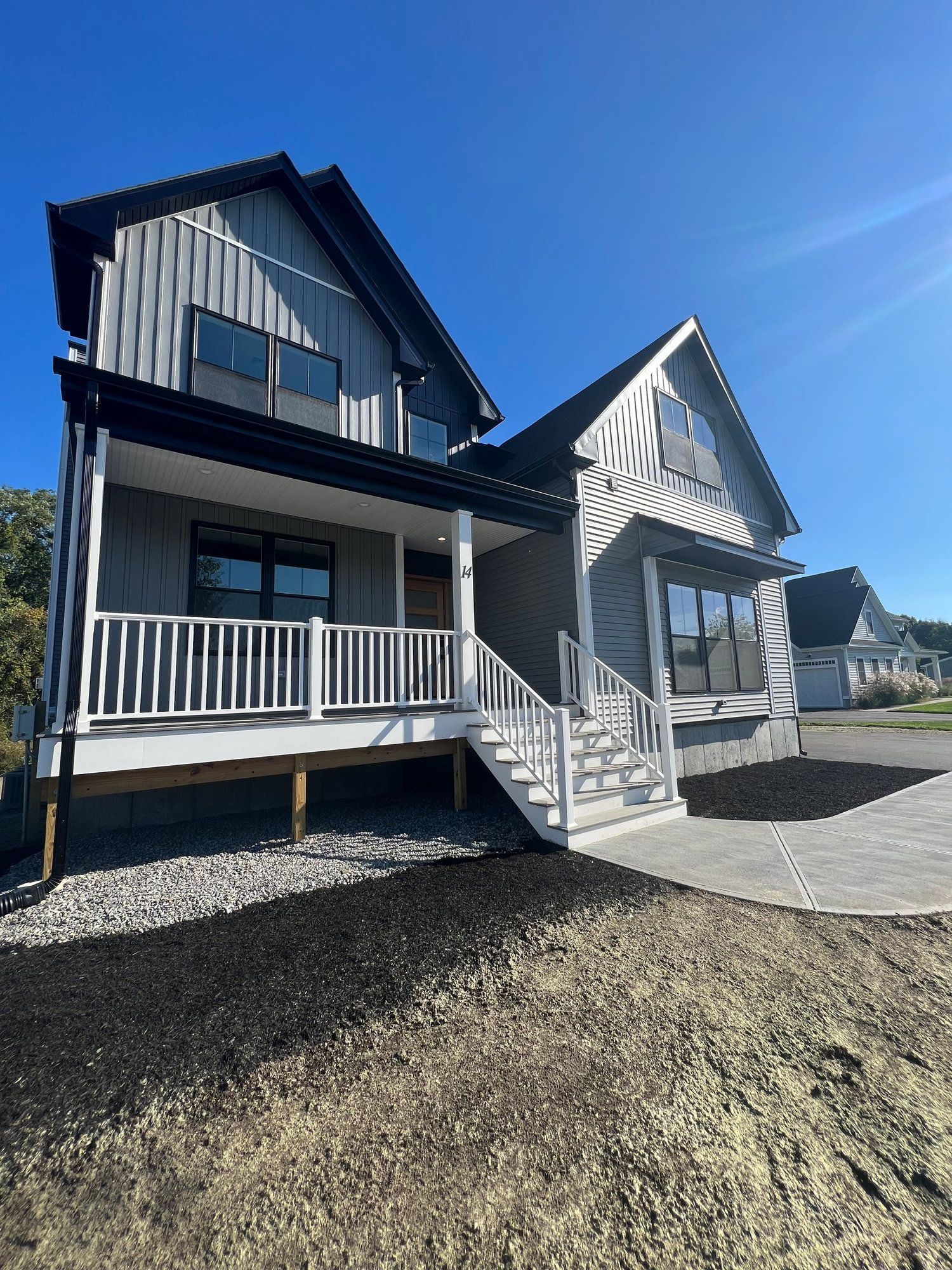 Modern two-story house with gray siding, white porch, and dark roof under a blue sky.