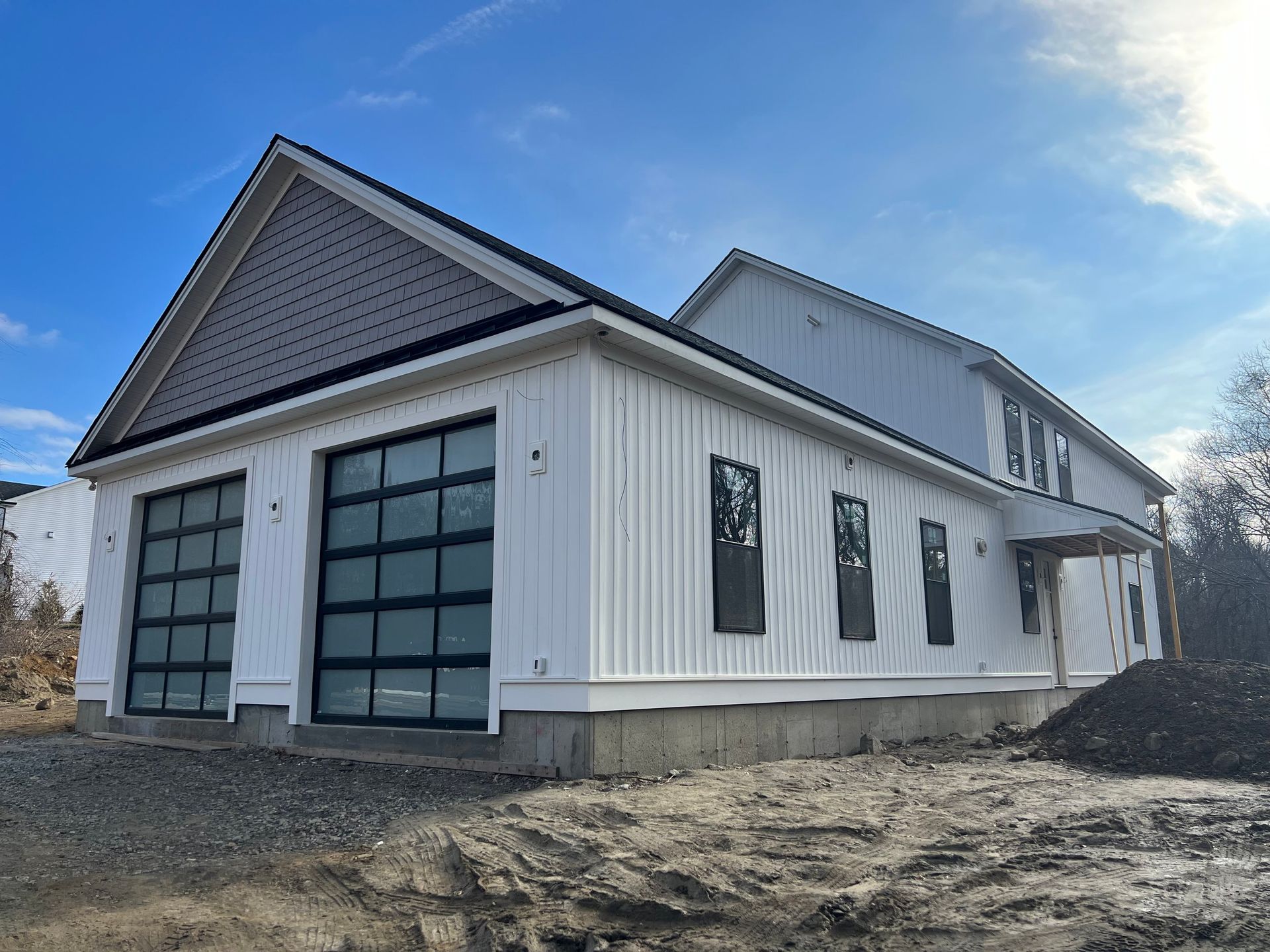 New construction house with white siding, glass garage doors, and dark roof against a blue sky.