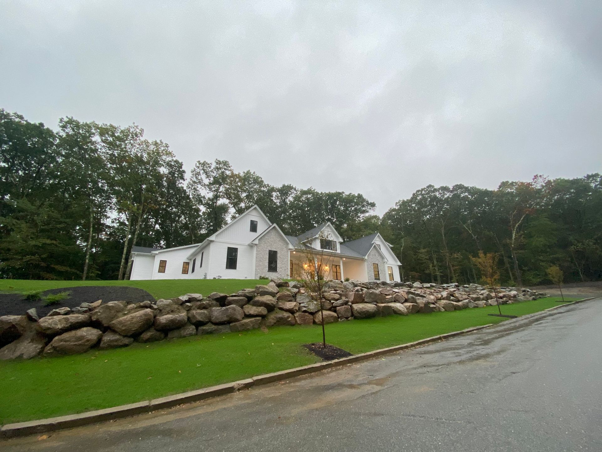 White house under construction, behind a stone wall, on a cloudy day. Green grass and trees surround it.