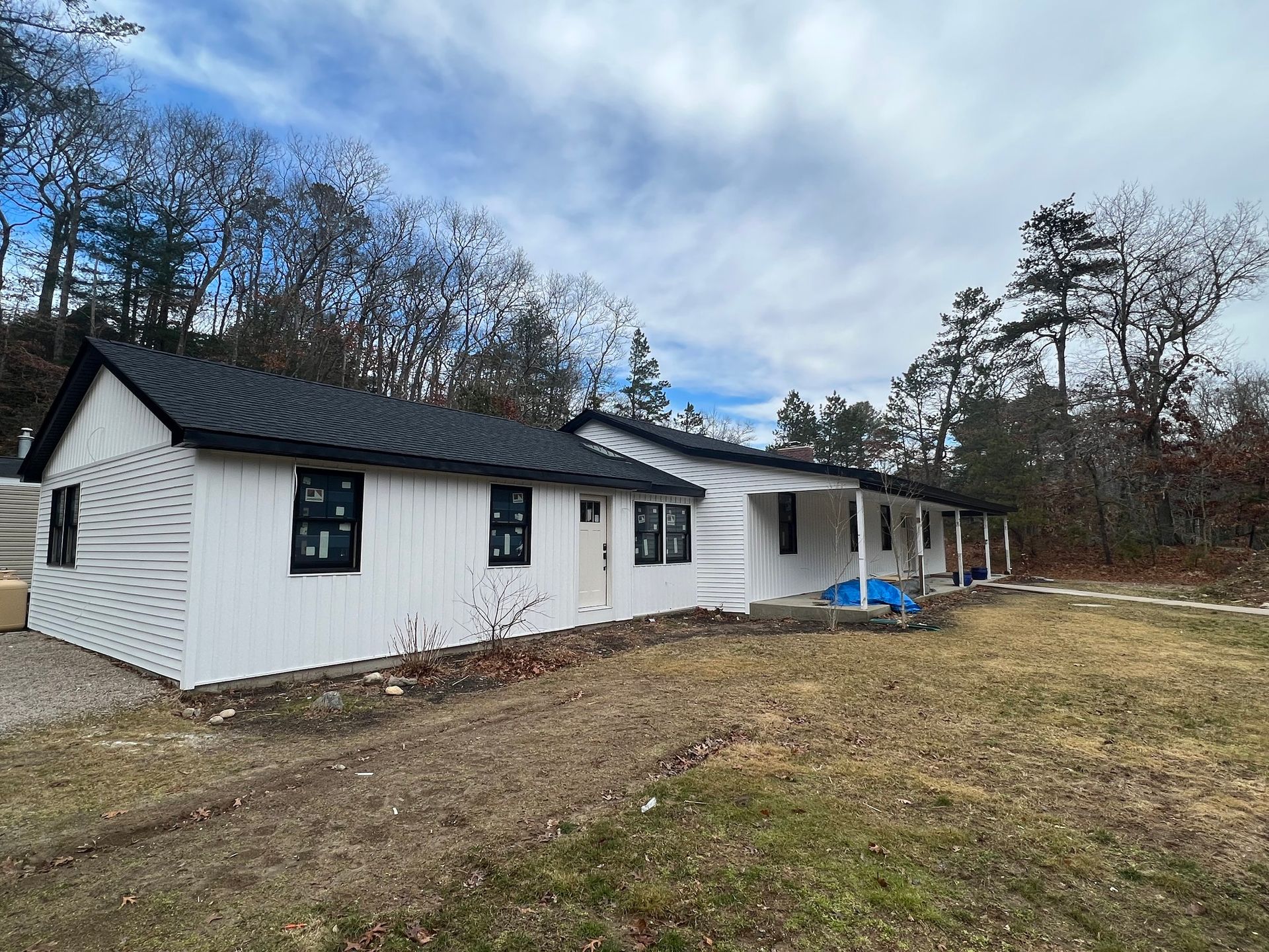 White house under construction with black roof and windows, set in a wooded area.