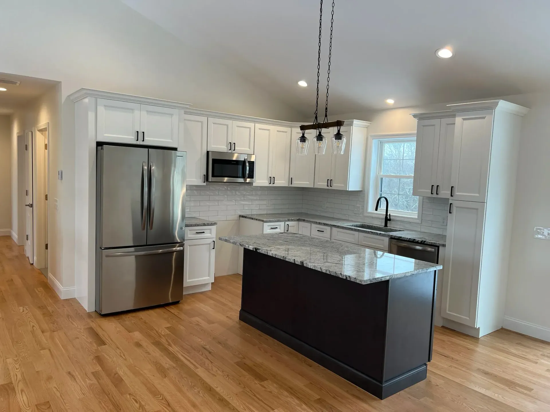 White kitchen with stainless steel appliances, dark island, and light wood floors.