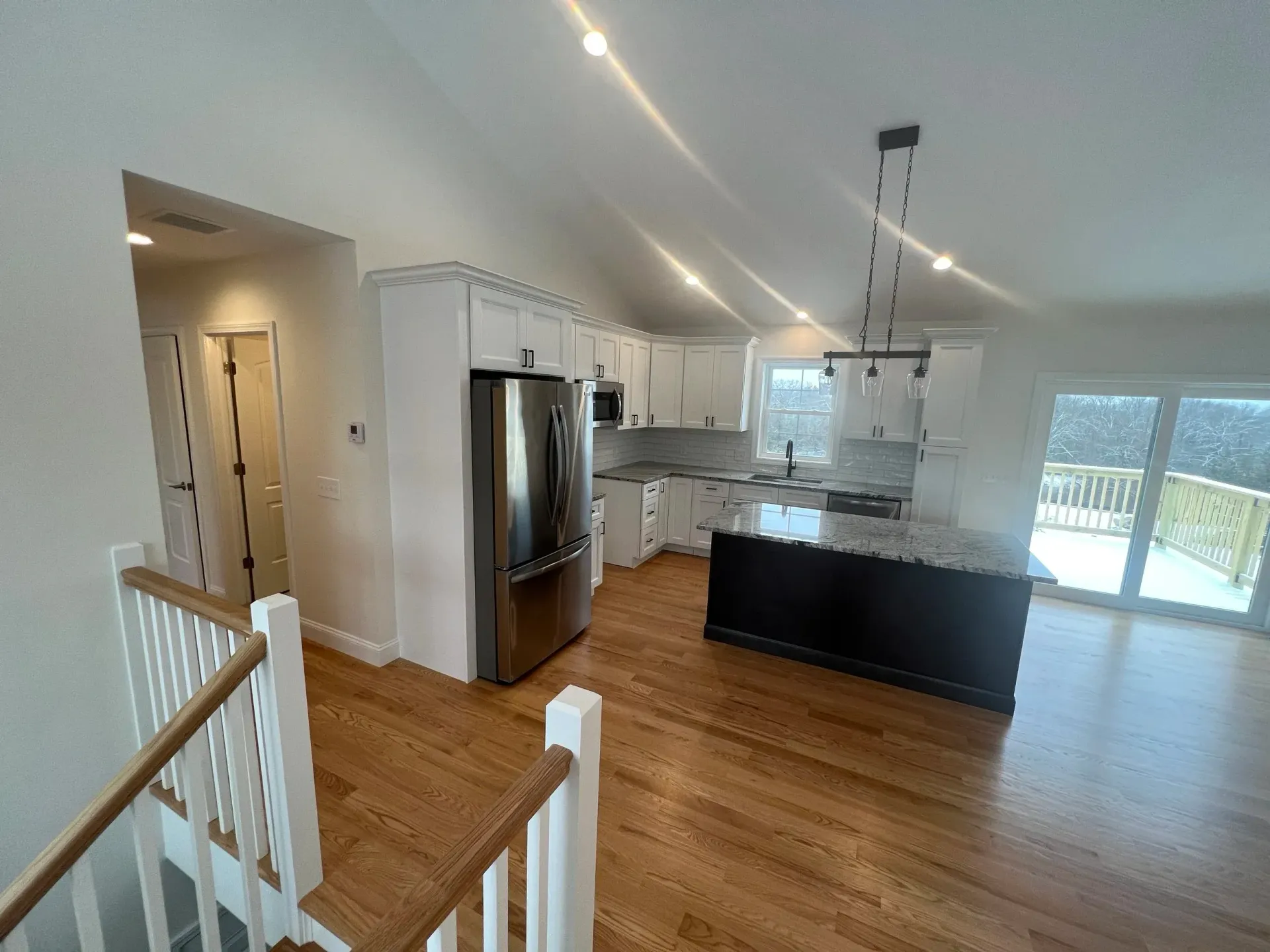 Open kitchen with white cabinets, stainless steel appliances, dark island, and wood floors.