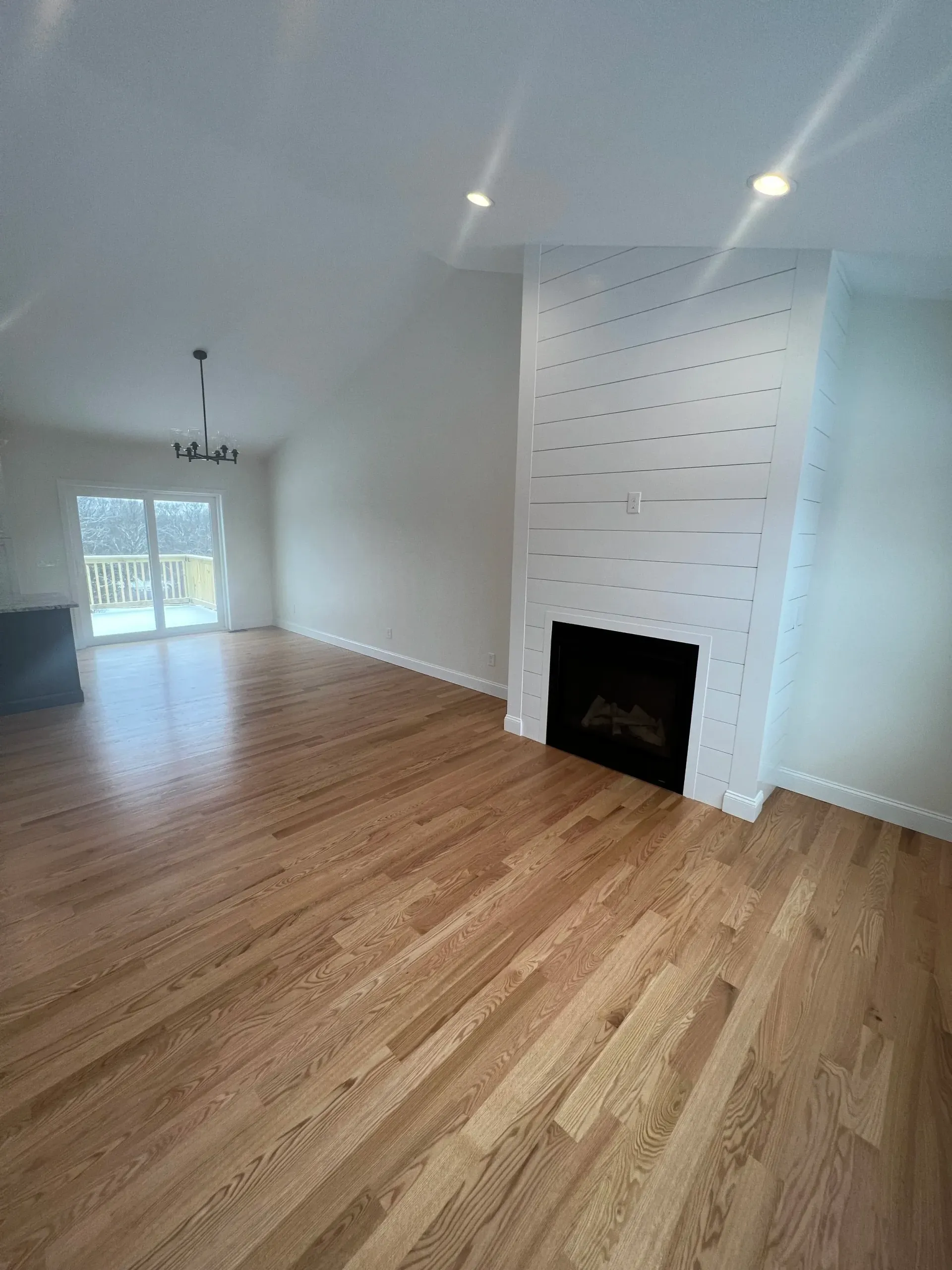 Empty living room with wood floors, white walls, and fireplace.