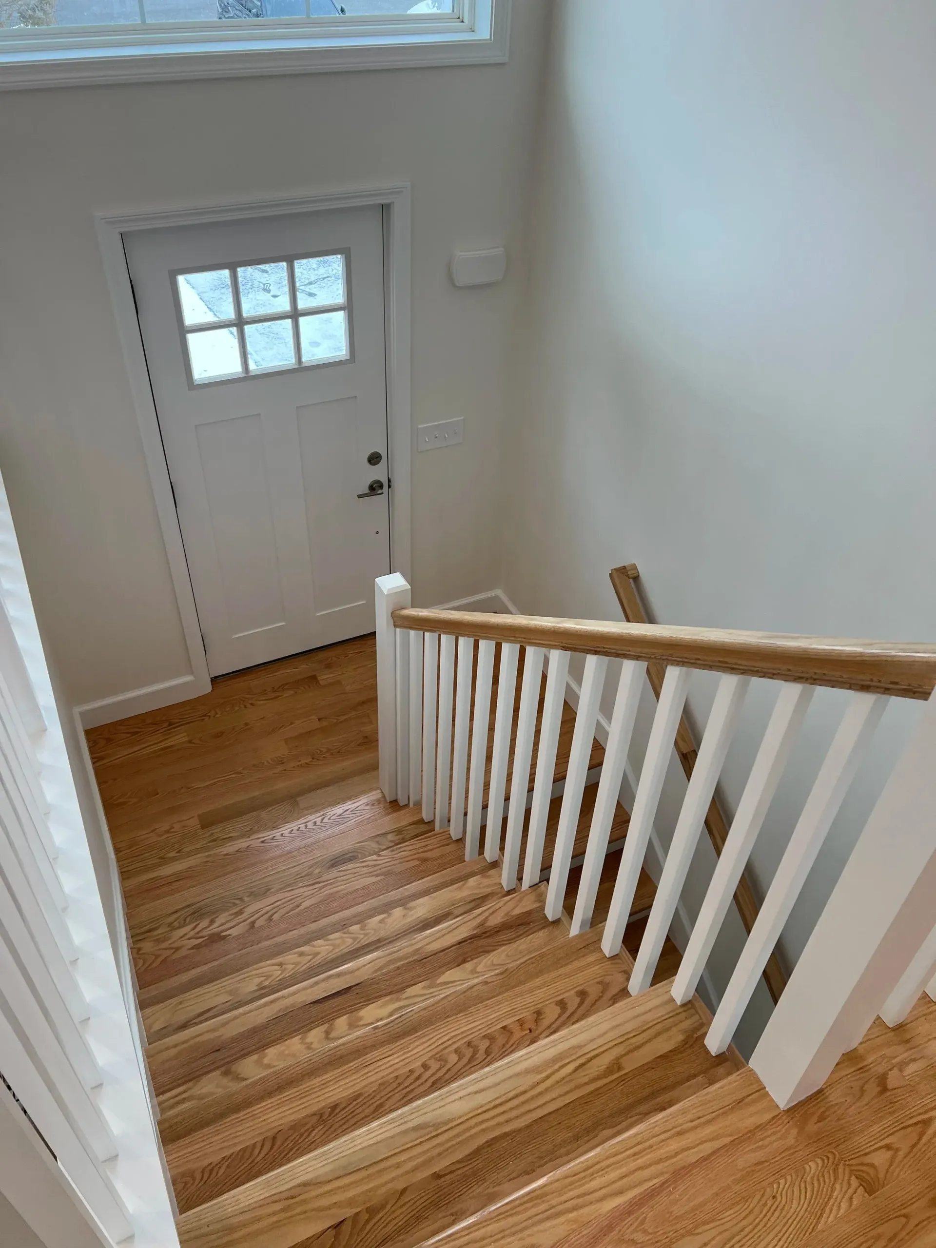Staircase leading down to a white door, with wooden floors and white railings.