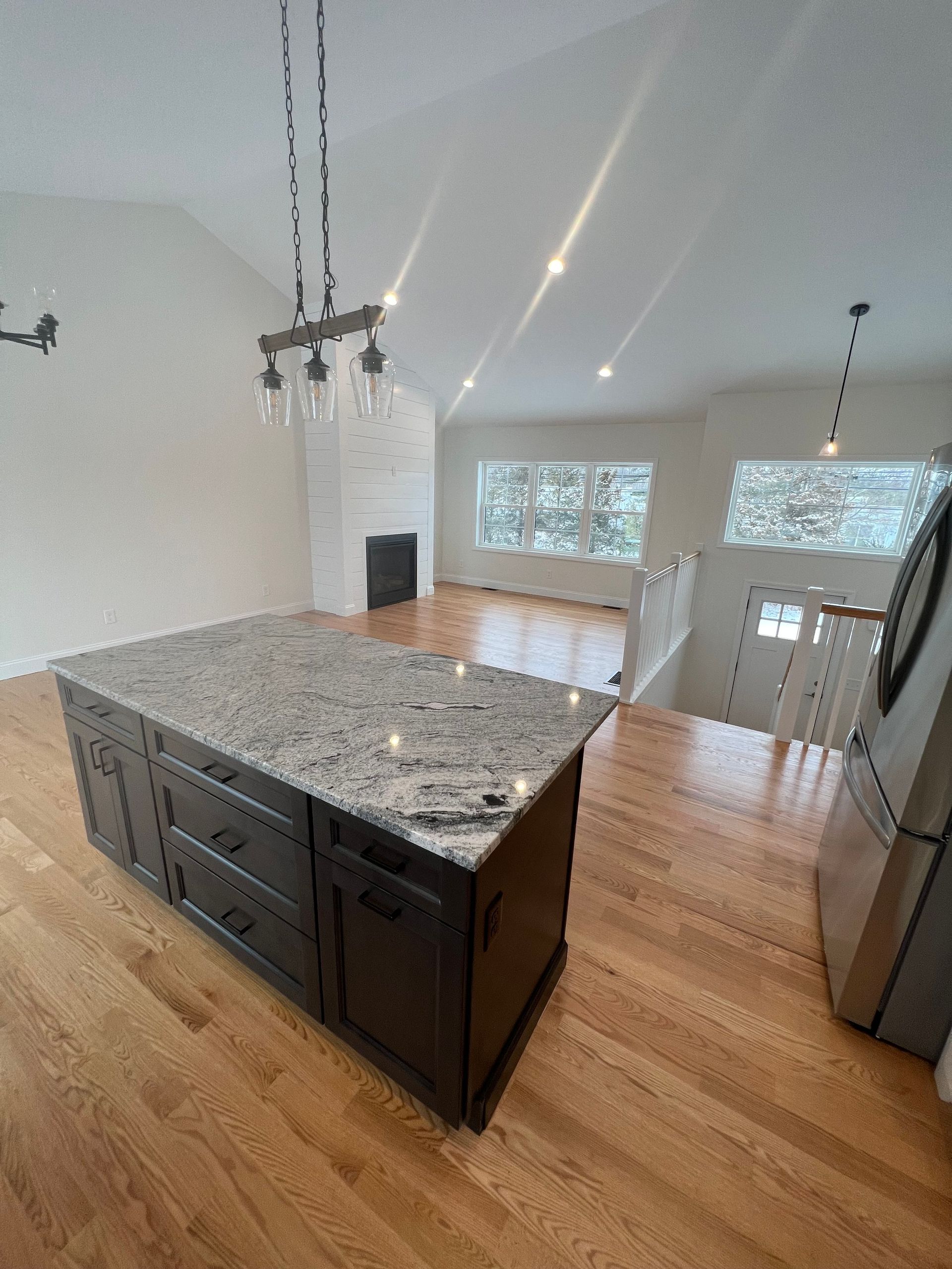 Kitchen with island, granite countertop, dark cabinets, and hardwood floors.  Light fixtures hang over the island.