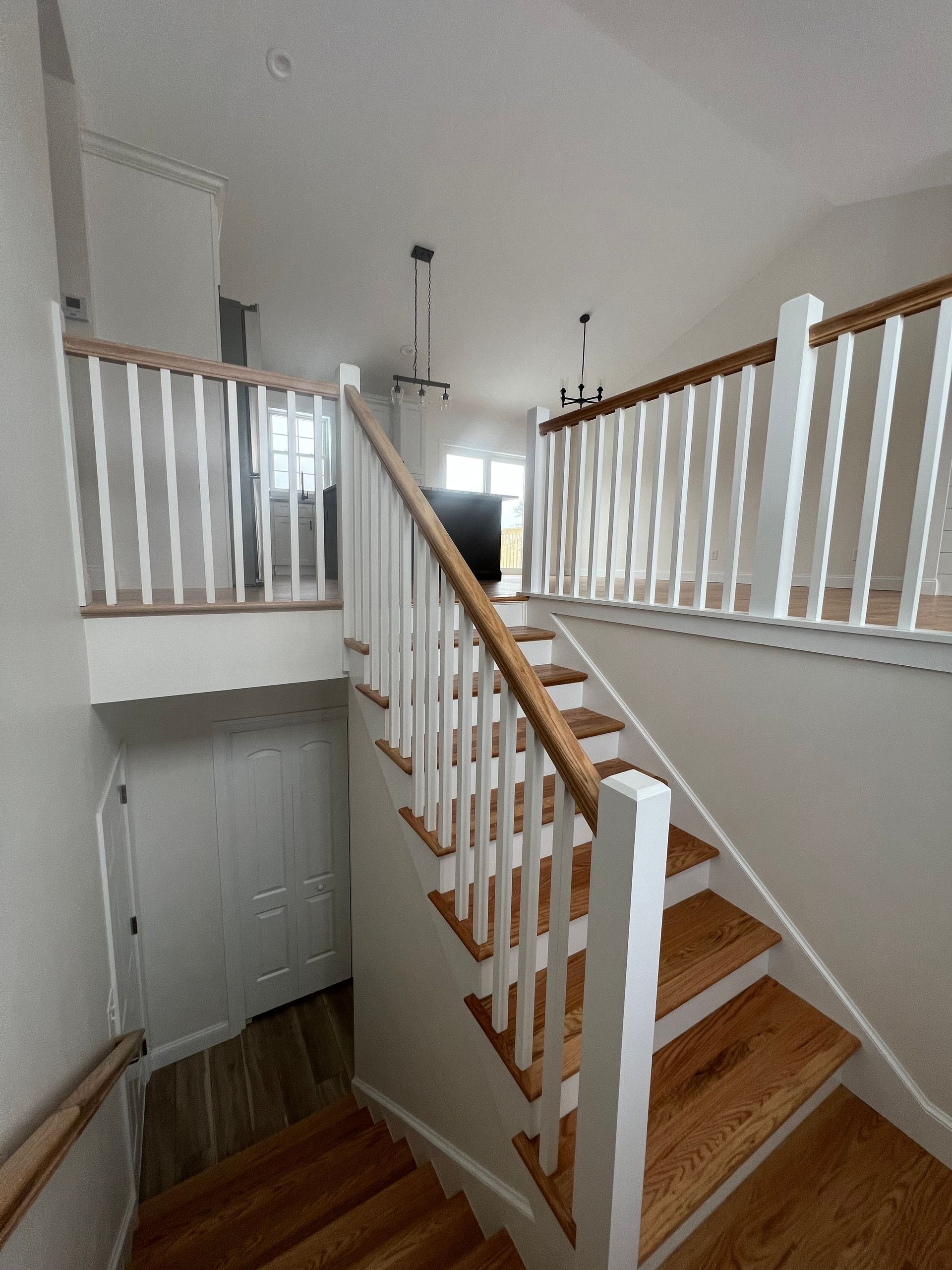 Wooden staircase with white railings, leading to a second floor. Door visible on the left.