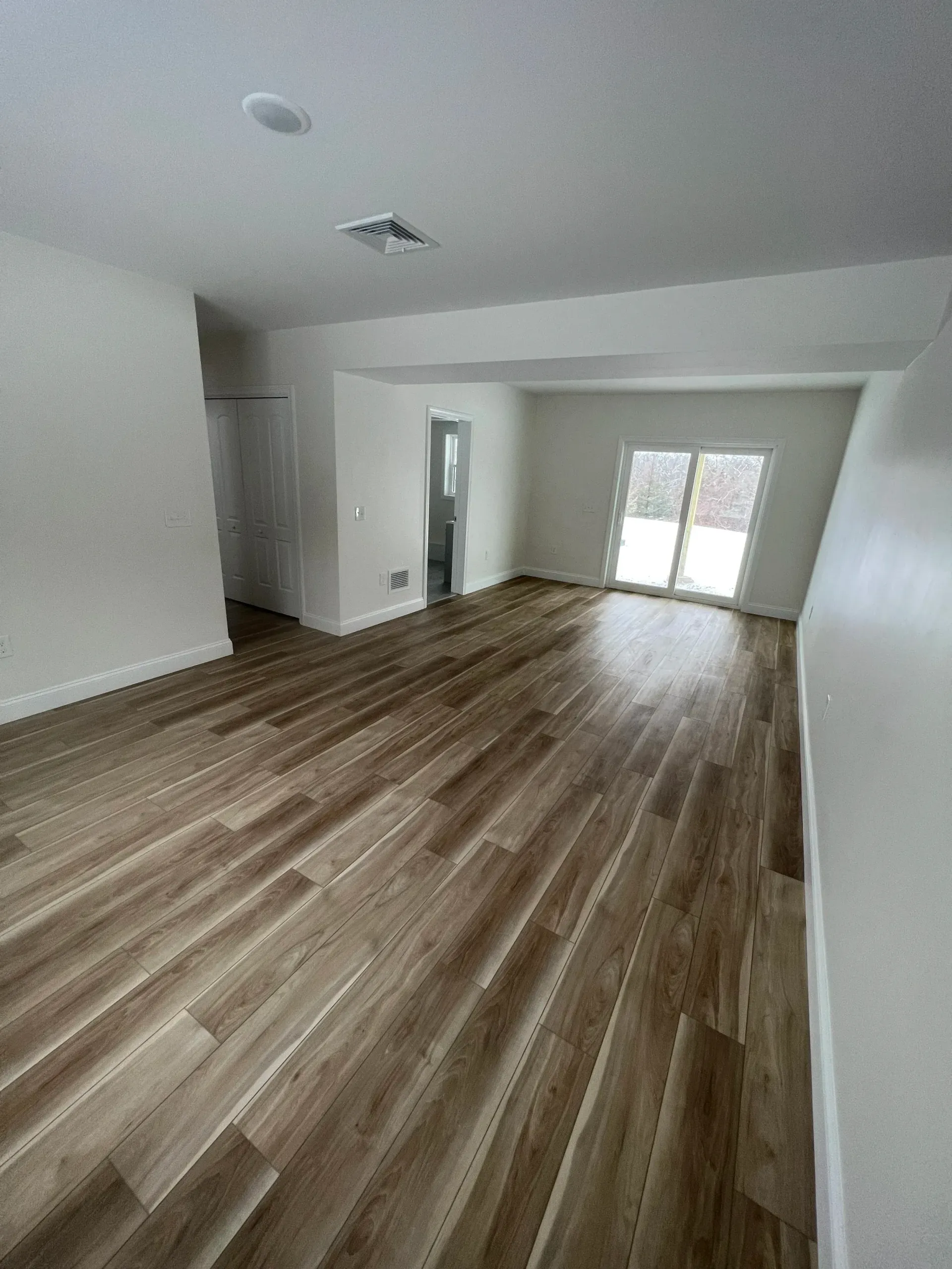 Empty living room with wood-look flooring, white walls, and a sliding glass door.