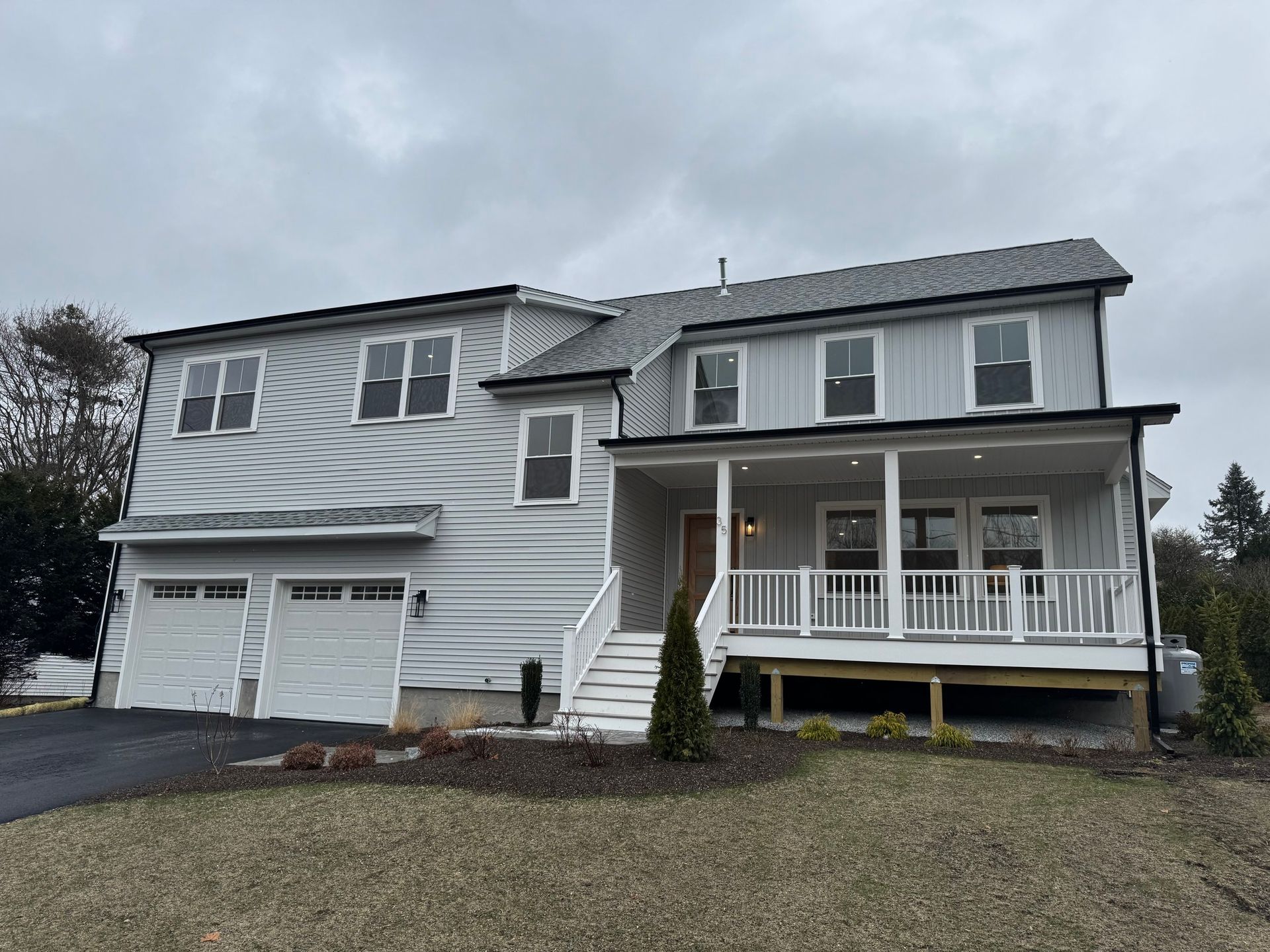 Two-story light gray house with a porch and a two-car garage under a cloudy sky.