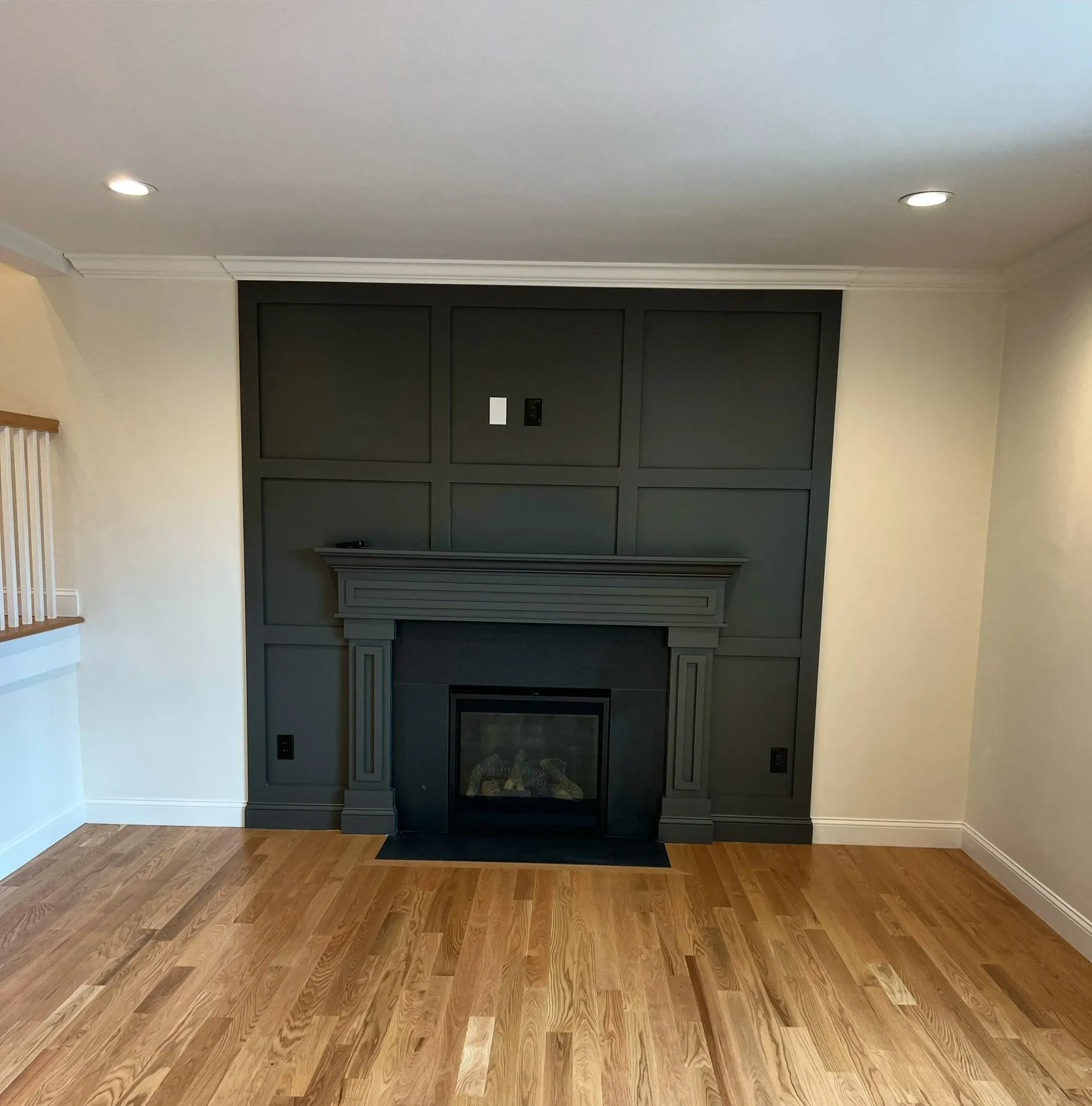 Dark gray fireplace with paneling, built-in black firebox, recessed lighting, hardwood floor.