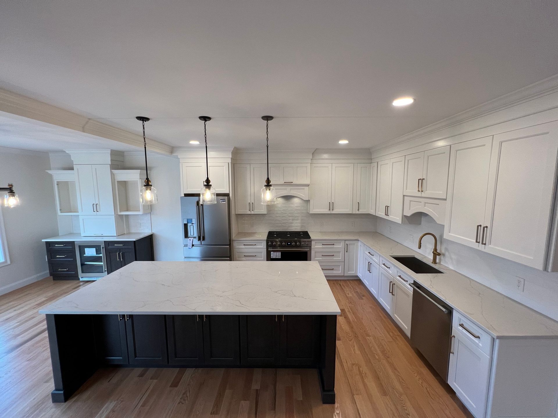 White kitchen with dark island and stainless steel appliances. Hardwood floors.