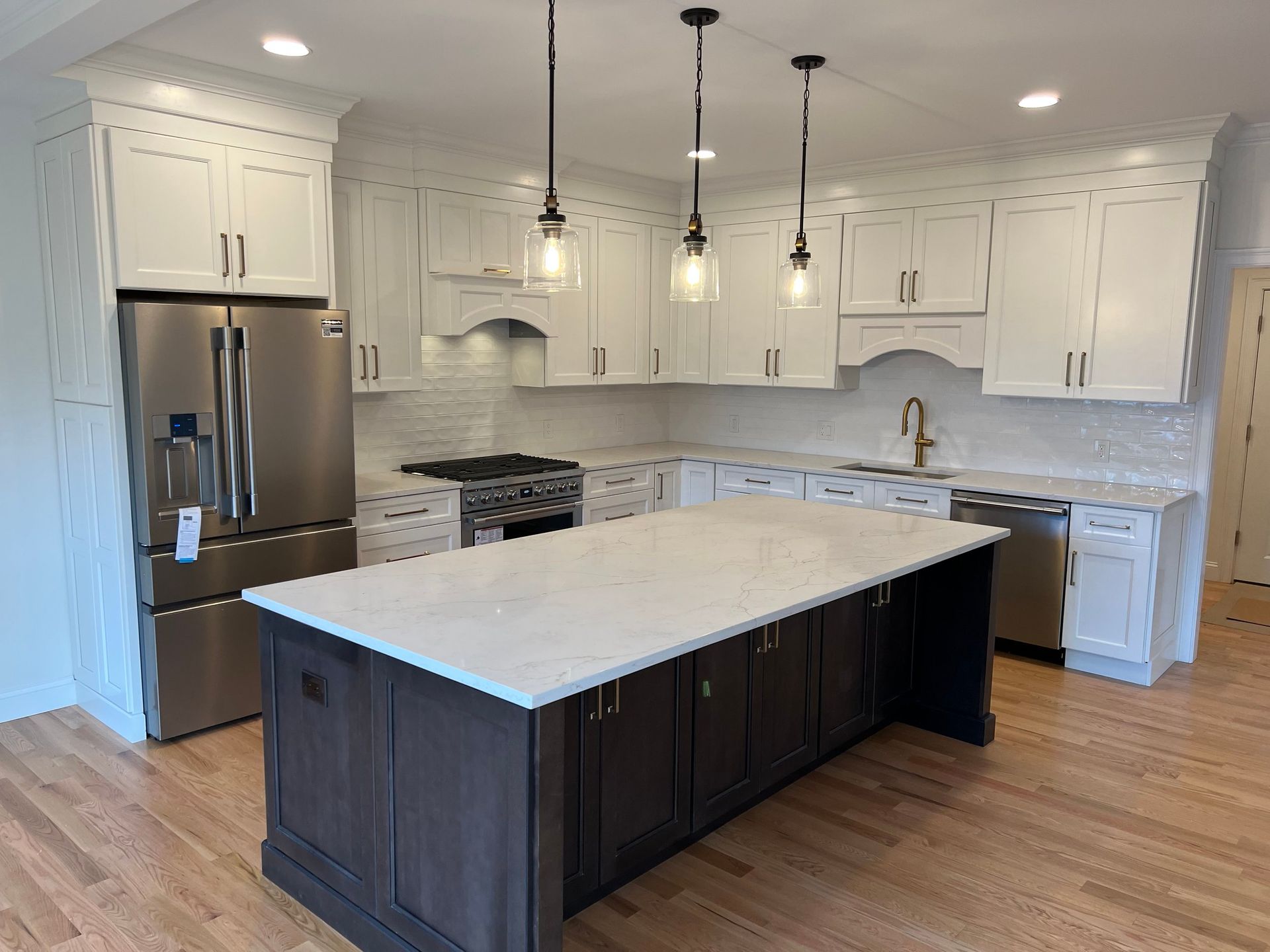 Modern kitchen with white upper cabinets, dark island, stainless steel appliances, and wood floor.