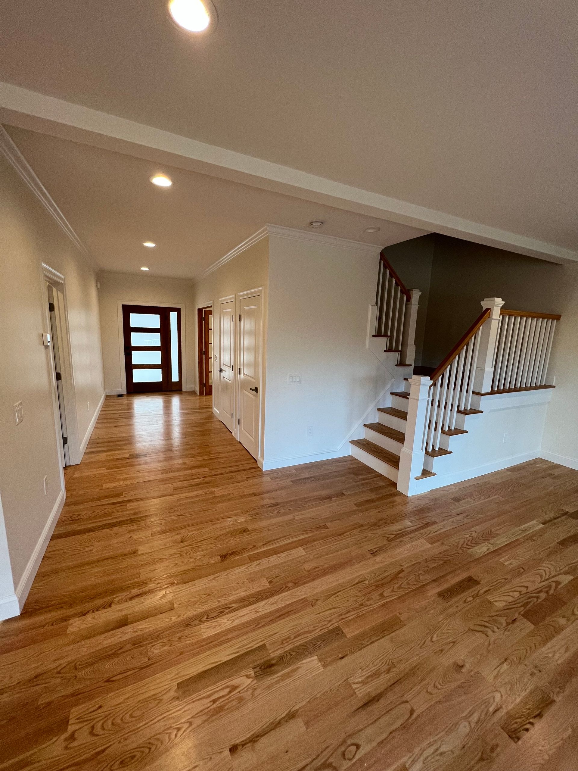Interior view of a house with hardwood floors, a staircase, and a long hallway with a front door.