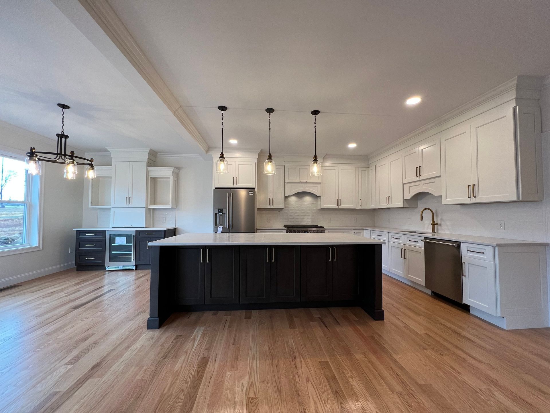 Spacious kitchen with dark island and white cabinetry, stainless steel appliances, and wood flooring.