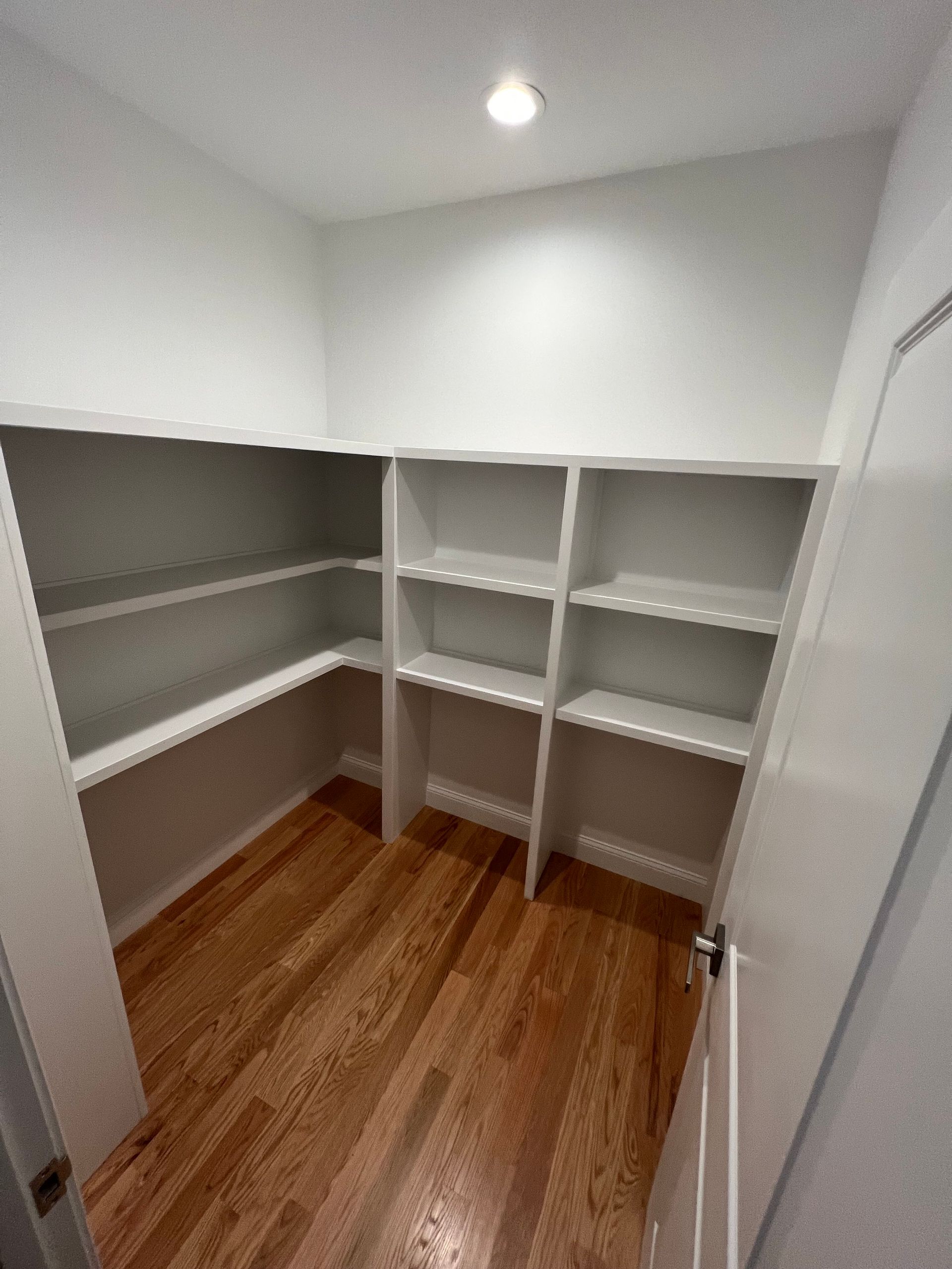 Empty white pantry with wooden floors and built-in shelves.