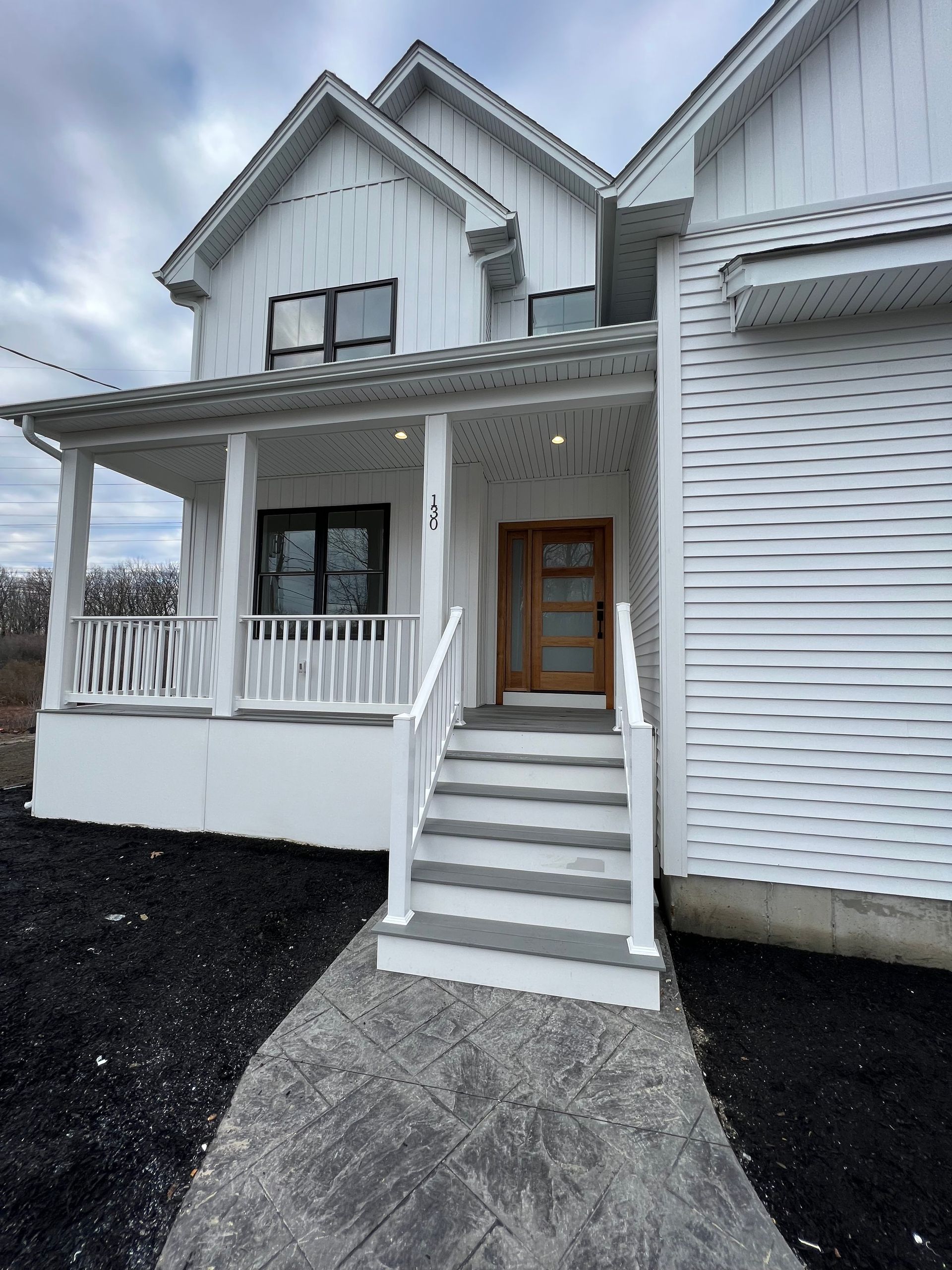 White house with a porch and wooden door. Gray steps lead to the entrance. Dark mulch surrounds.