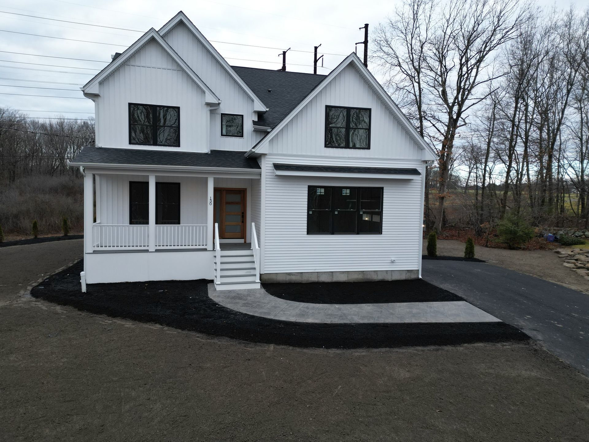White two-story house with black trim and dark roof; front porch; black mulch landscaping; asphalt driveway.