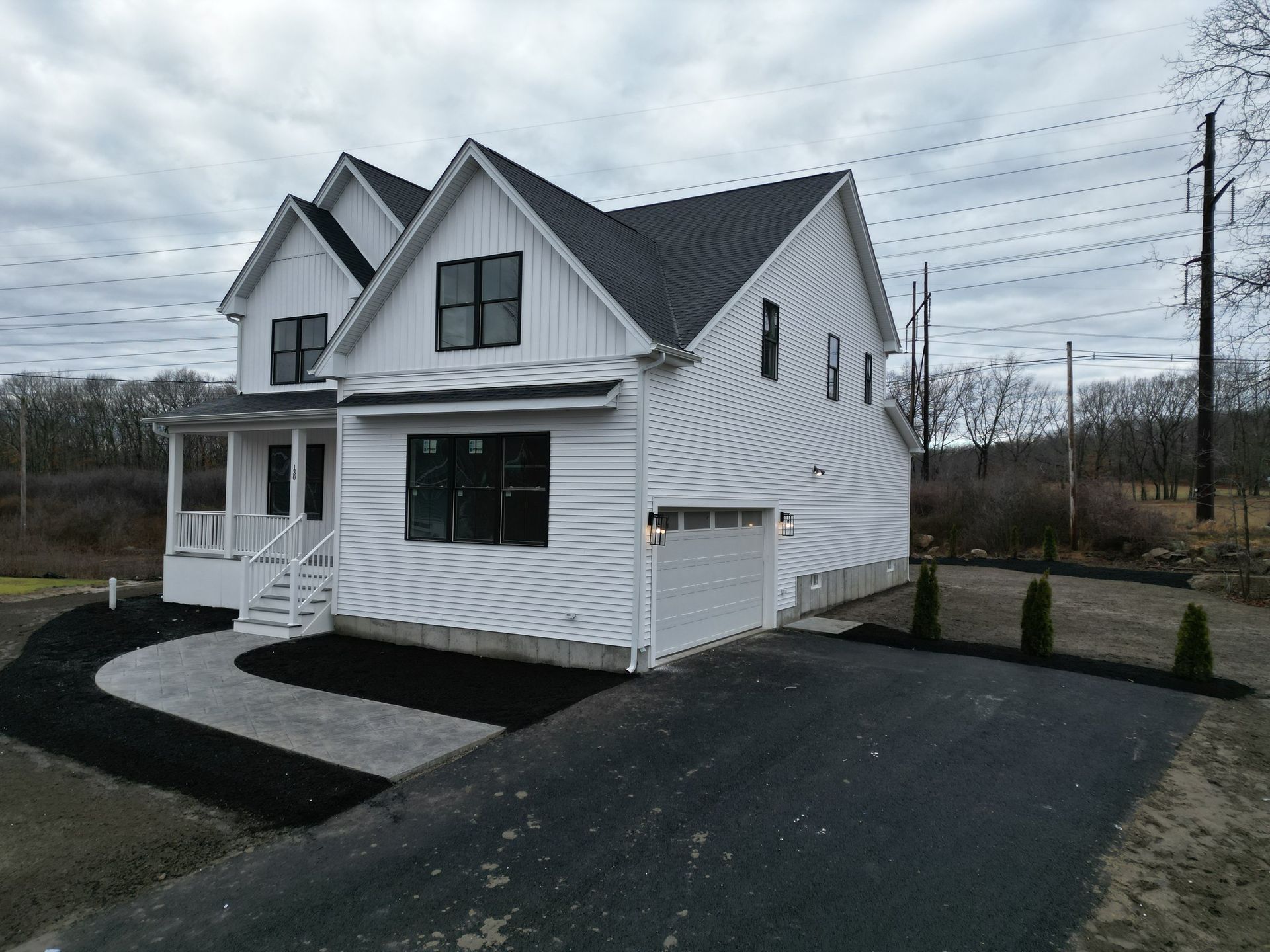 White farmhouse with black trim and a black asphalt driveway on a cloudy day.