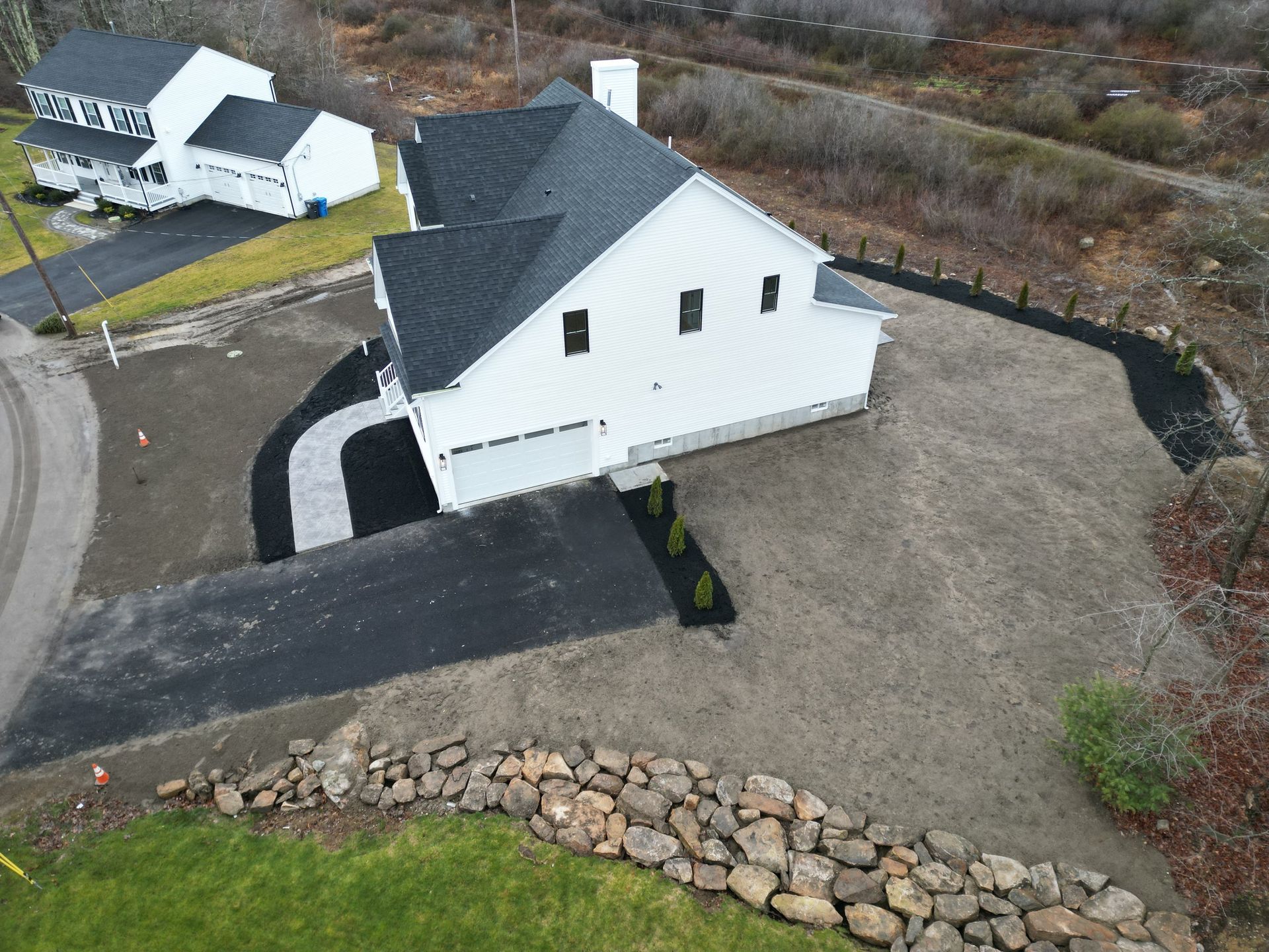 White house with black roof, driveway, and landscaping; view from above.