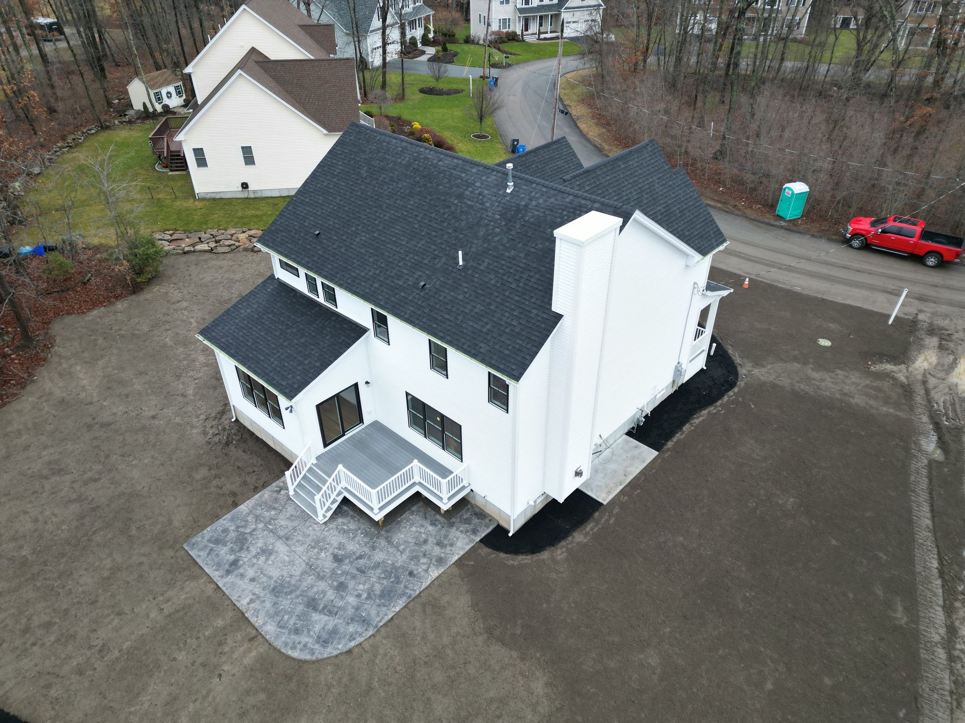 Aerial view of a white two-story house with a black roof and gray patio, surrounded by gravel and landscaping.