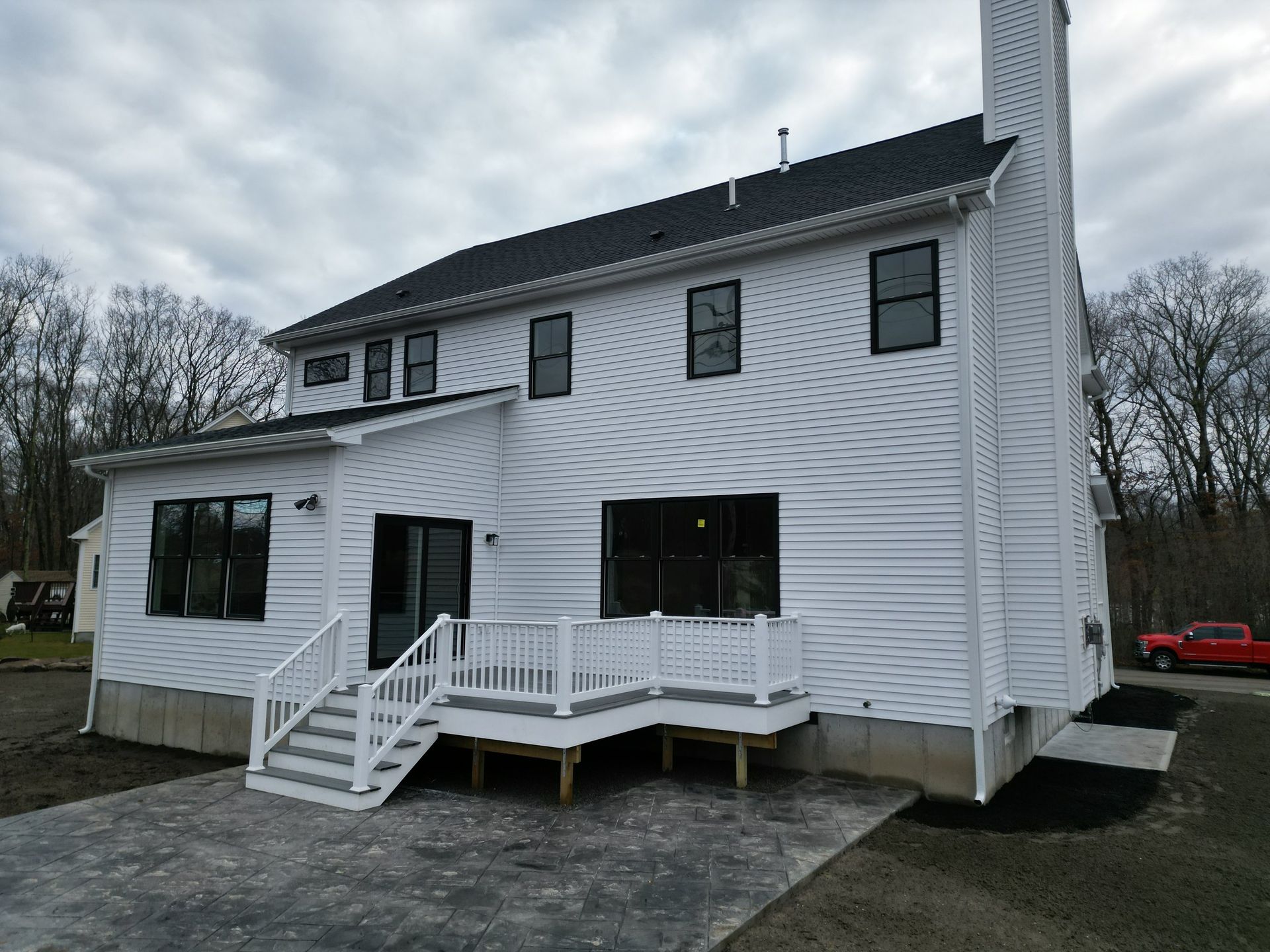 White two-story house with black-framed windows, deck, and chimney under a cloudy sky.