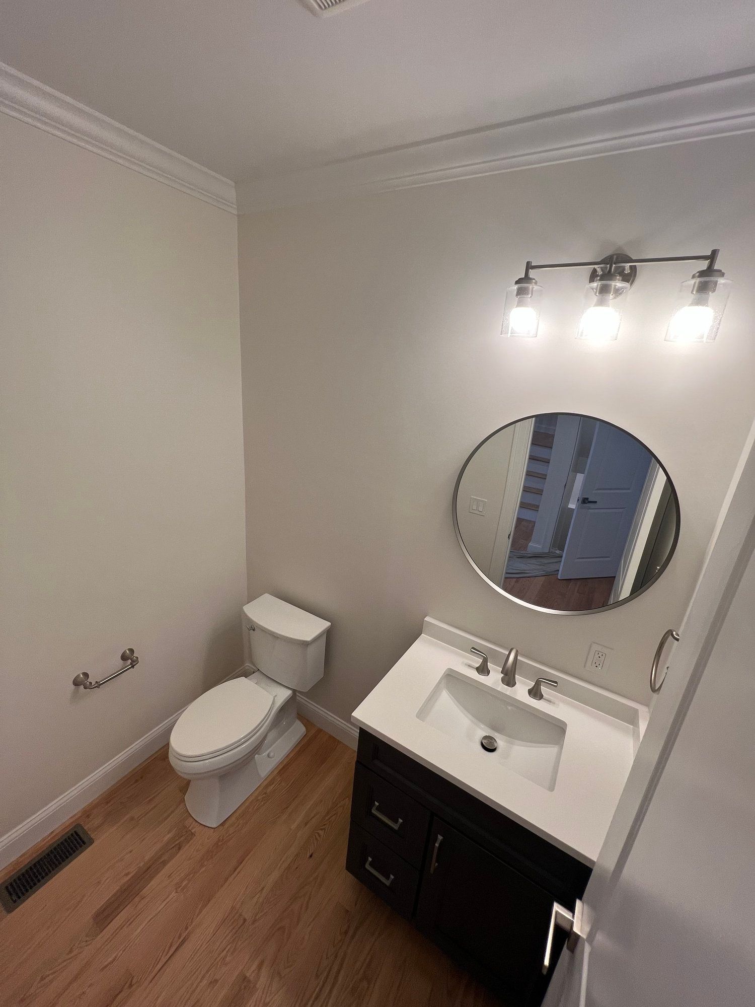 Bathroom with toilet, sink, mirror, and light fixture, light wood floor, white walls and trim.