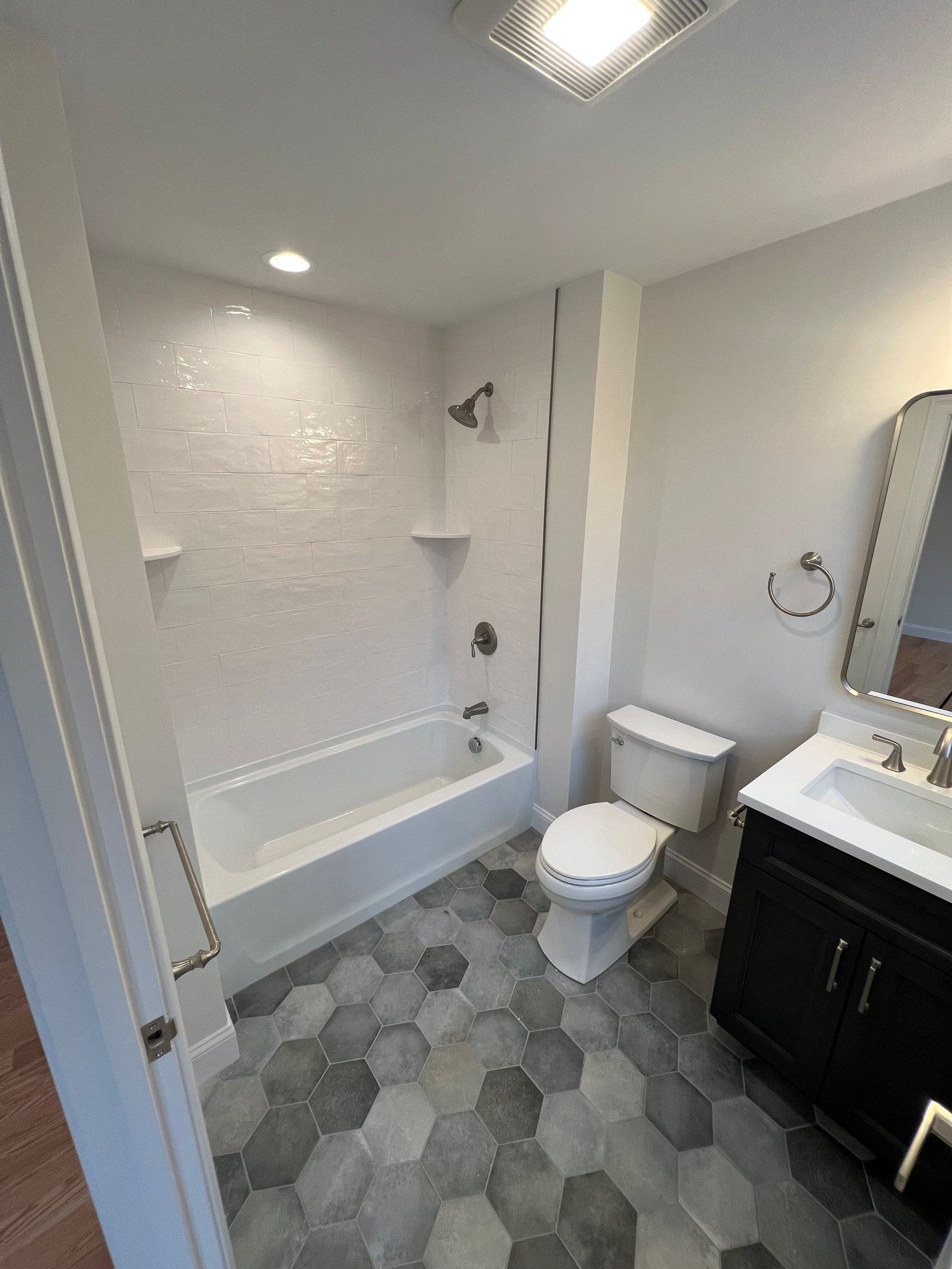 Bathroom with white walls, hexagon floor tiles, tub, toilet, vanity, and mirror.