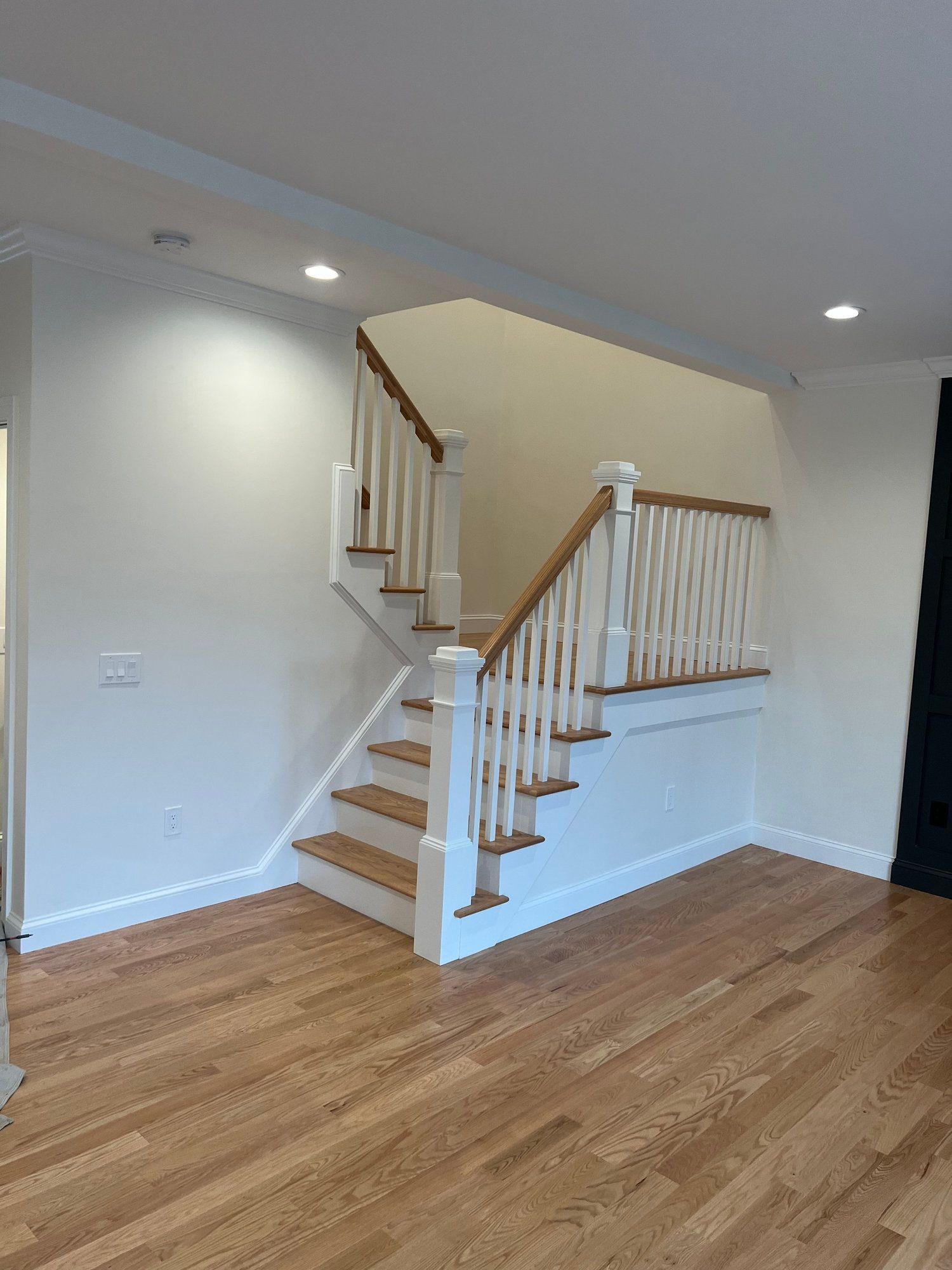 Wooden staircase with white banisters and oak flooring in a brightly lit room.