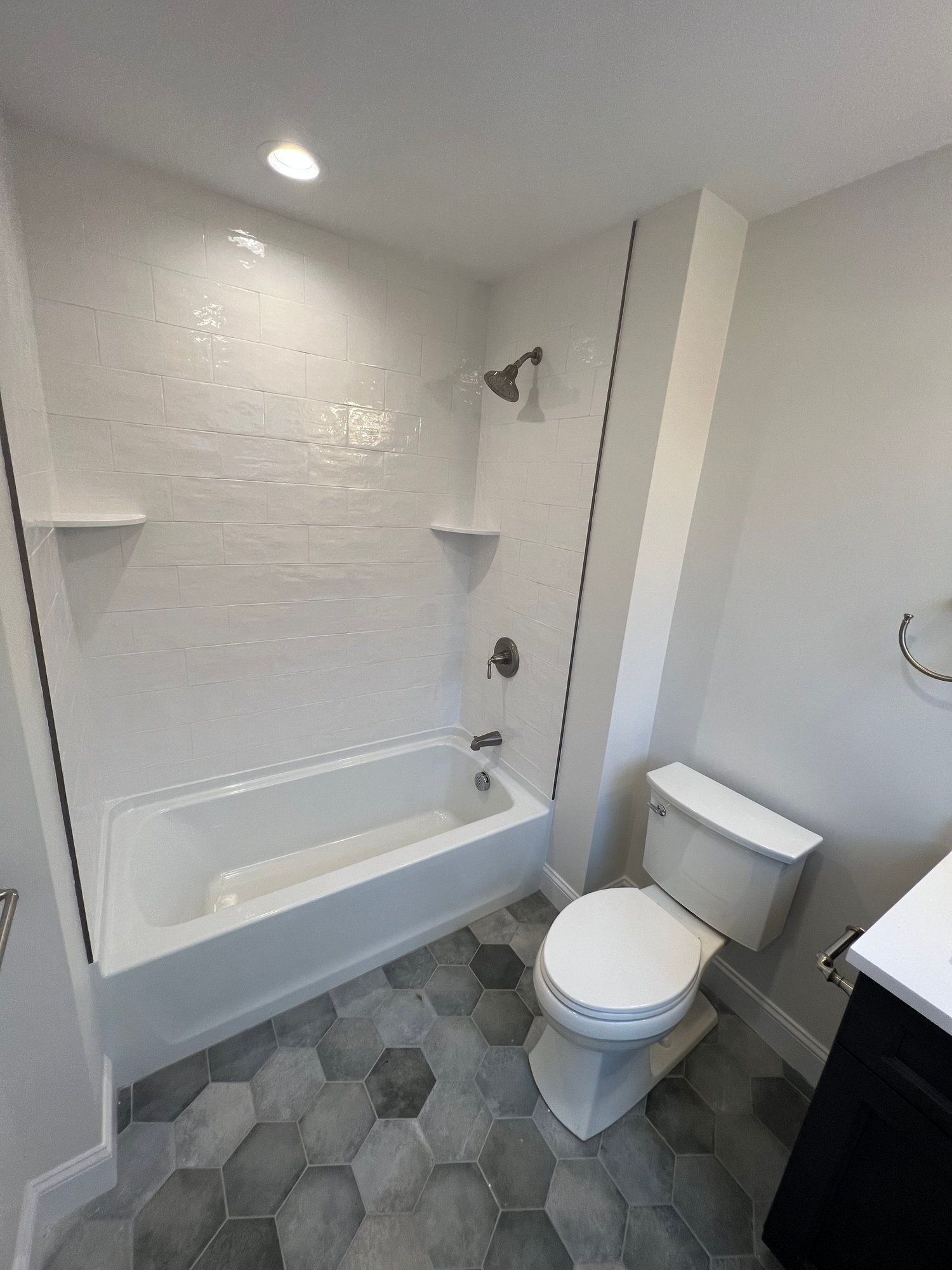 Modern bathroom with white tub and walls, gray hexagonal floor tiles, and a white toilet.