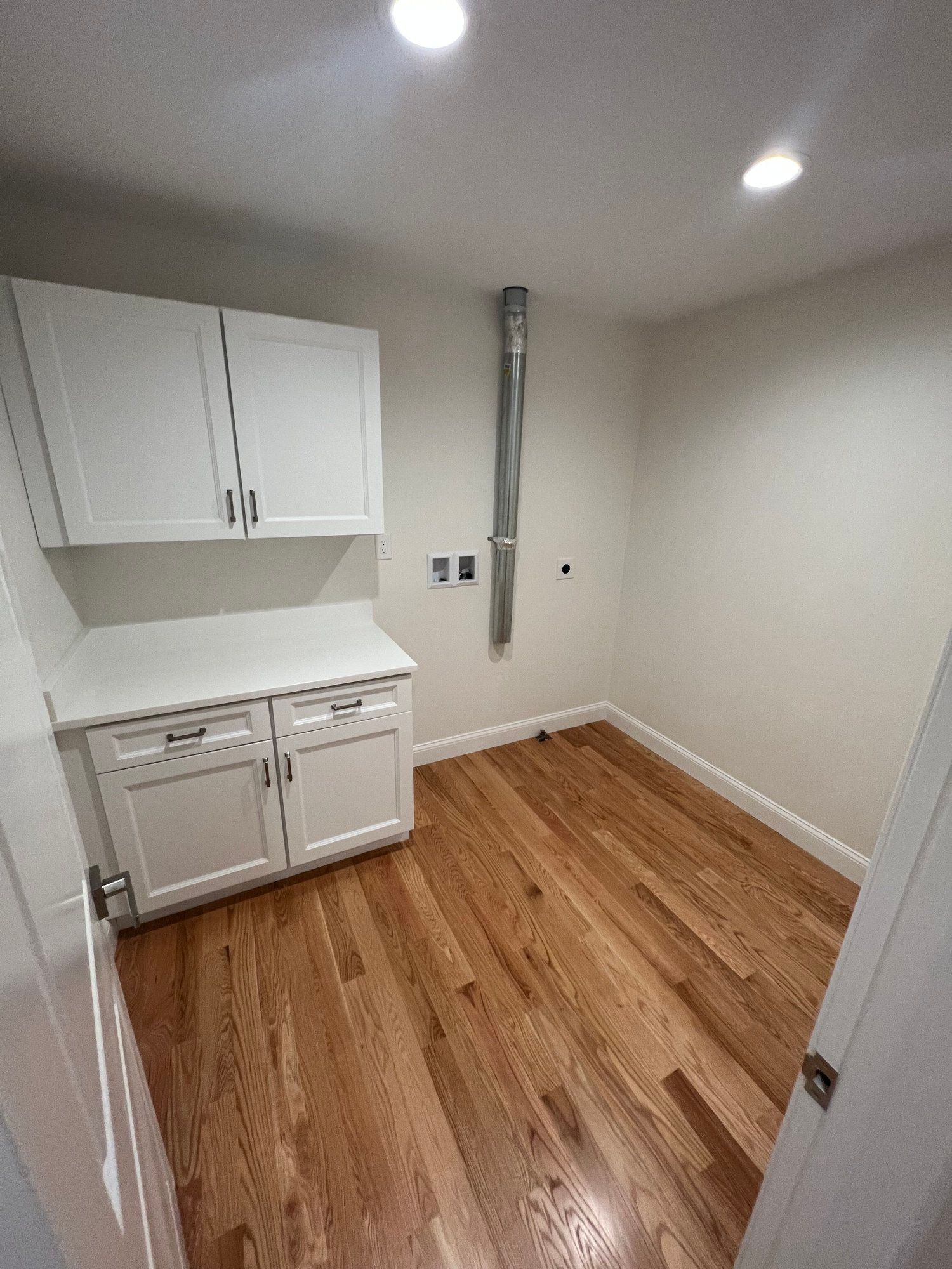 Laundry room with white cabinets, countertop, wooden floor, and a vent.