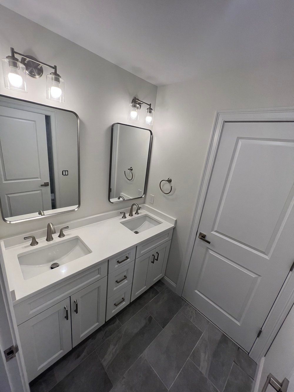 Bathroom with white double vanity, mirrors, and gray tile floor.