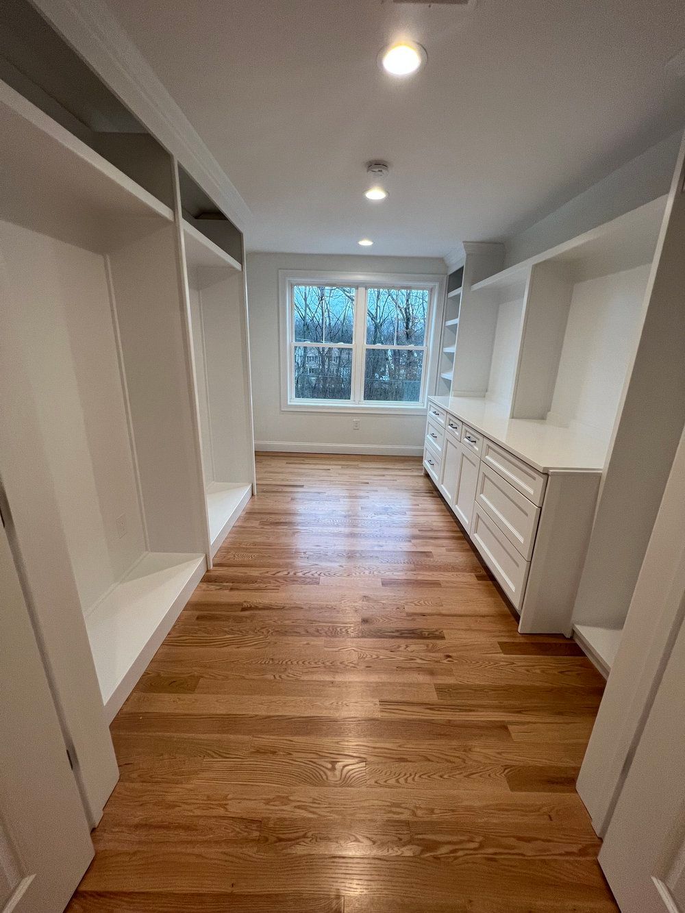 Walk-in closet with white shelves and drawers, wood floor, and window.