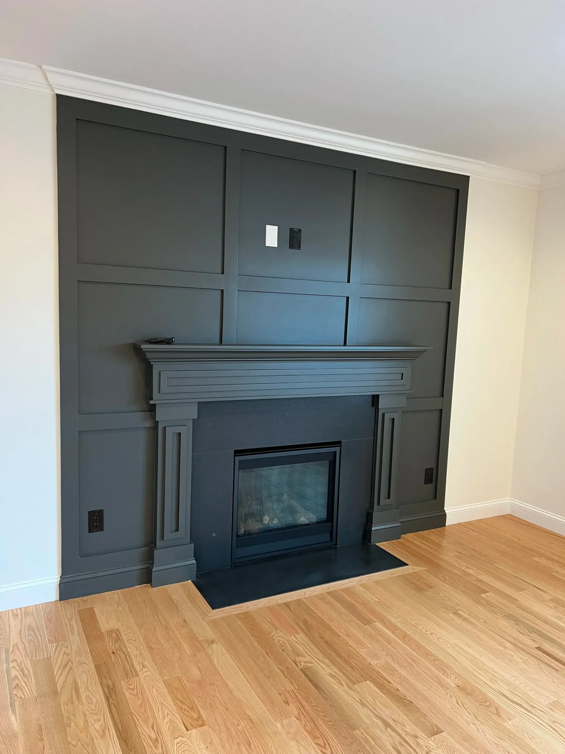 Dark gray fireplace with paneling, built-in black firebox, and light wood flooring.