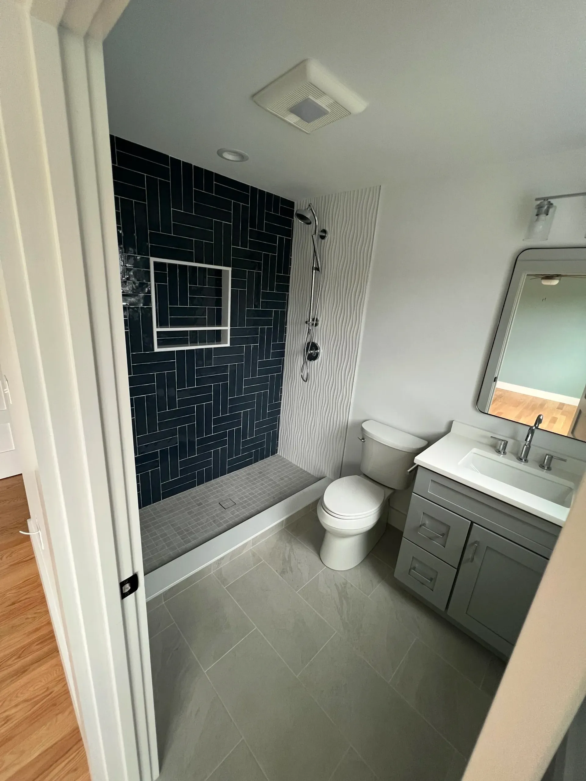 Newly renovated bathroom with gray floor tiles, blue and white shower tiles, gray vanity, and white toilet.
