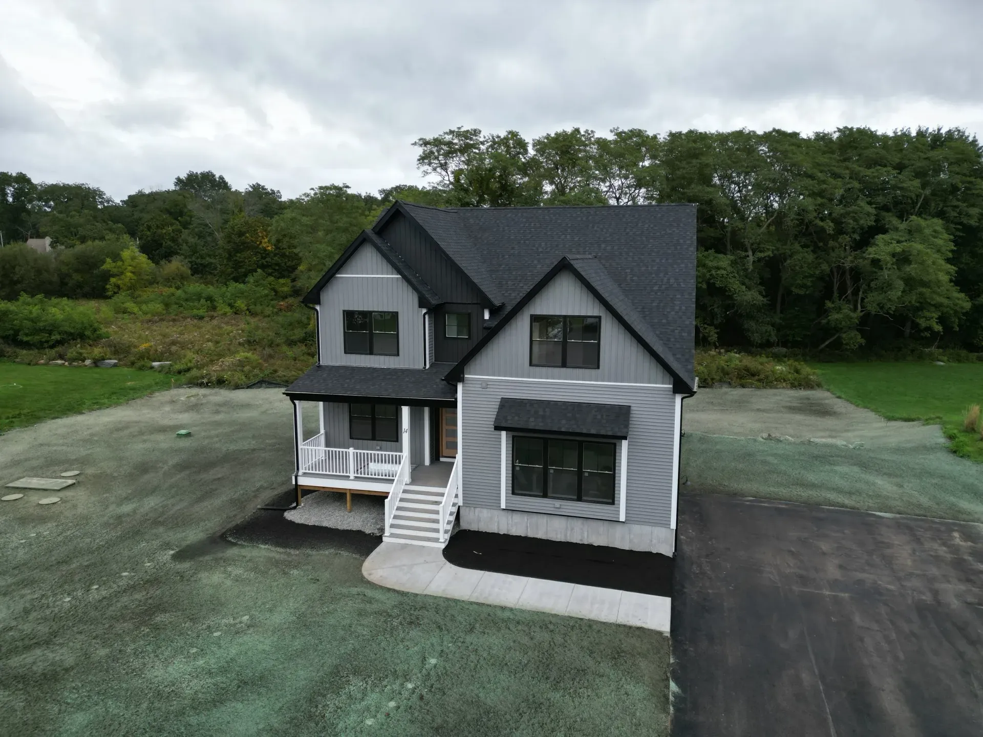 Modern two-story house with gray siding, black roof, and dark trim, set on a grassy lot.