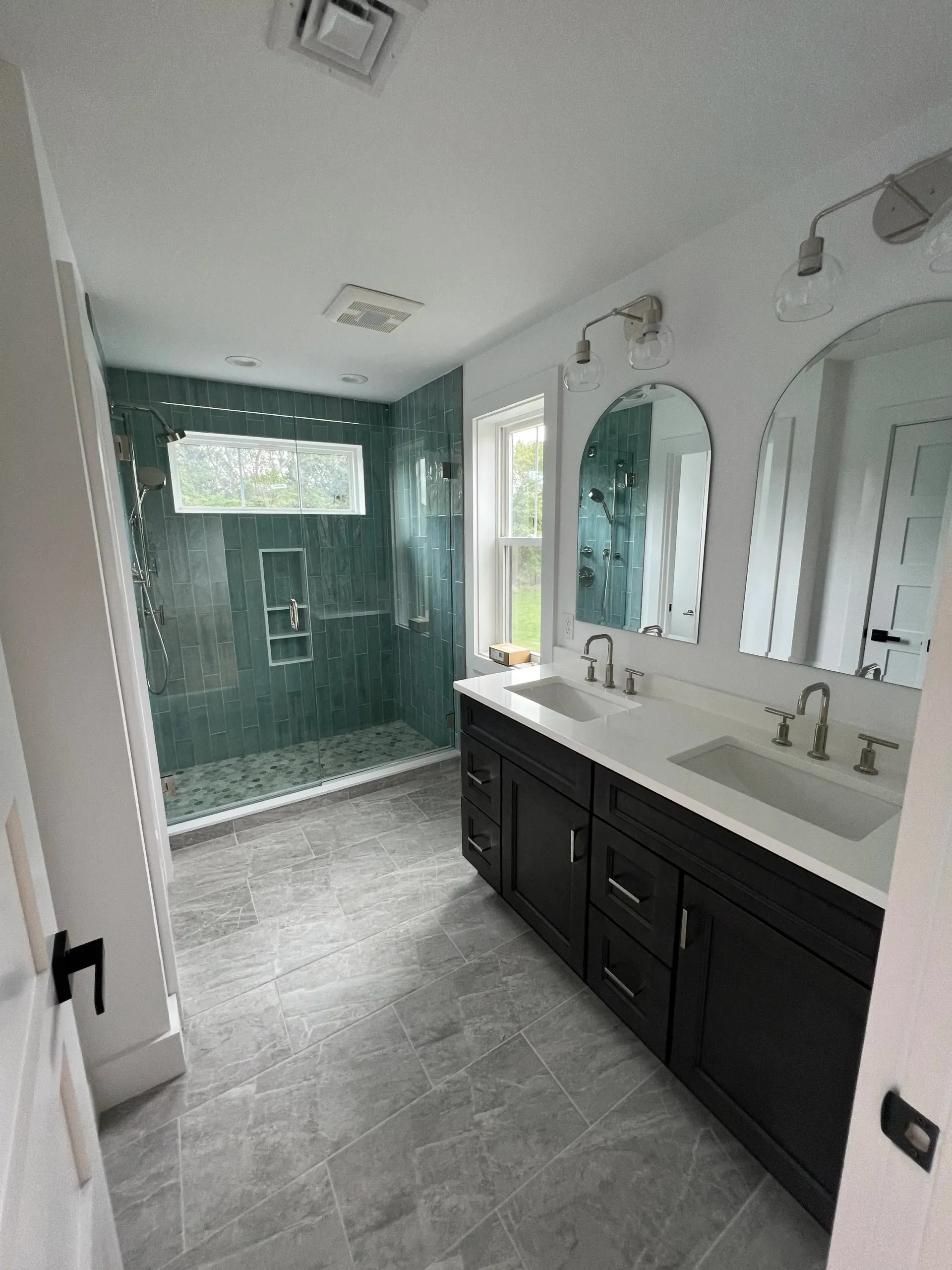 Modern bathroom with teal tile shower, dark vanity, and arched mirrors.