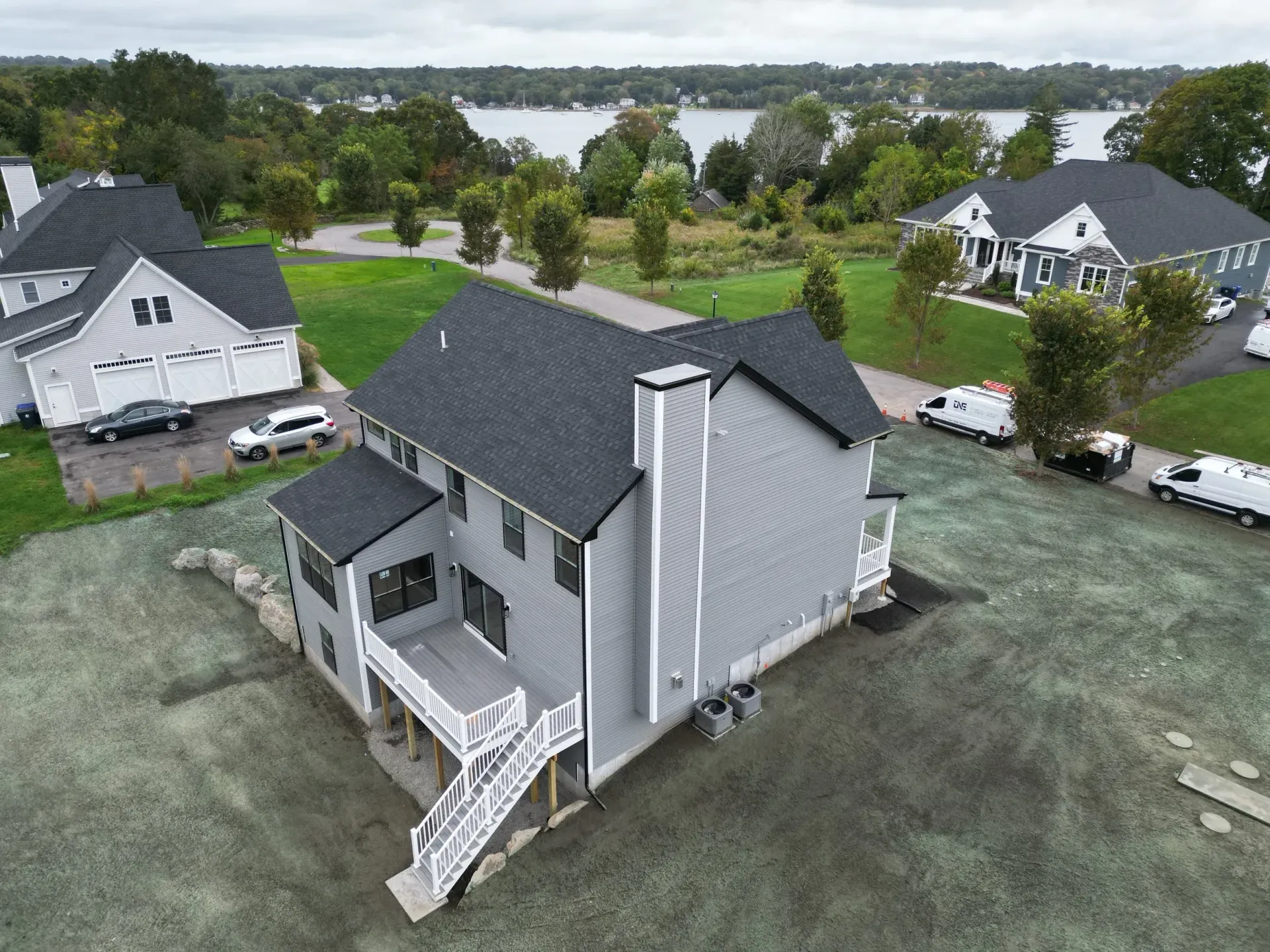 Aerial view of a gray house with a black roof, deck, and chimney near a lake.