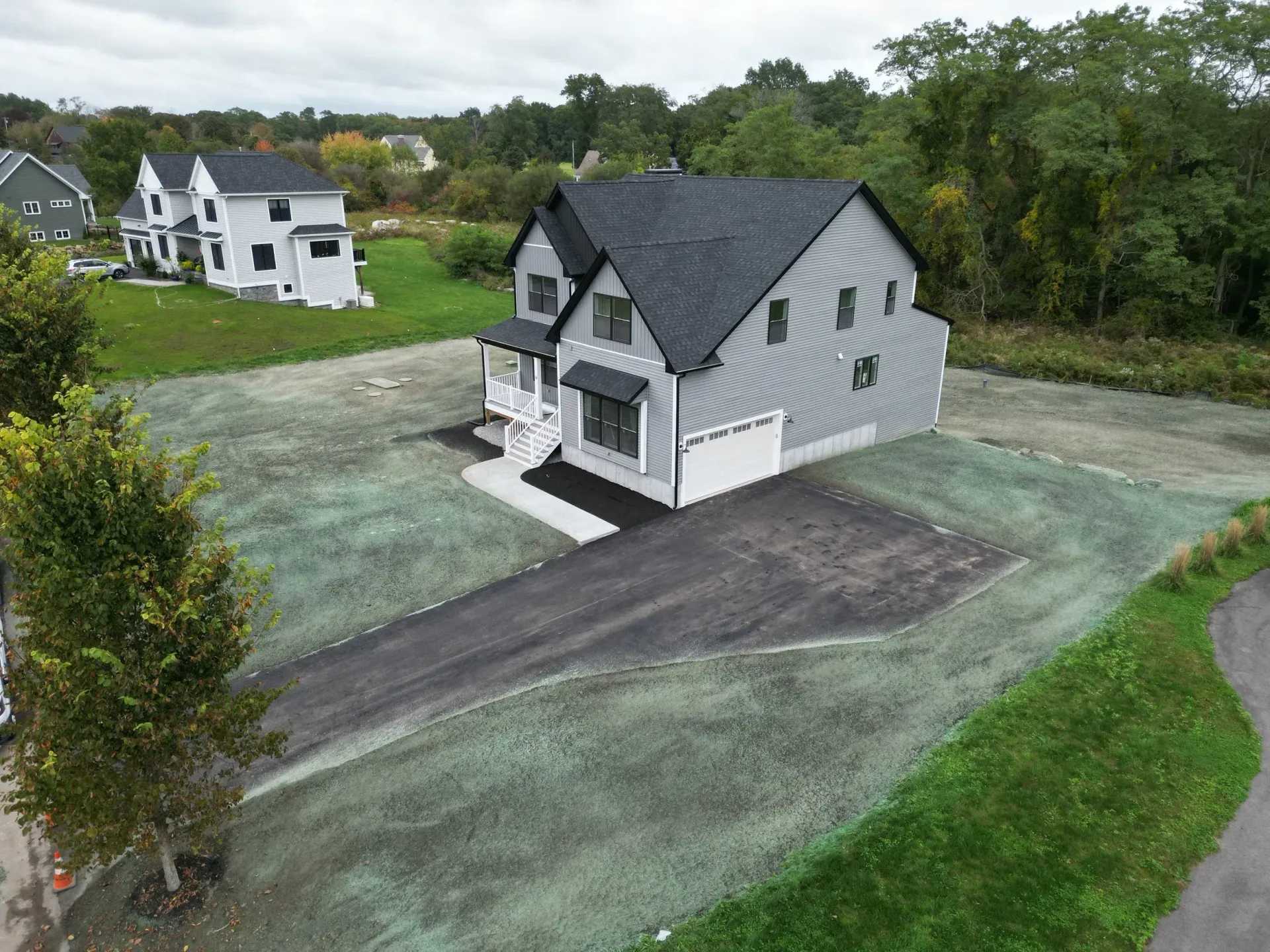 New two-story house with gray siding, black roof, and paved driveway on a grassy lot.