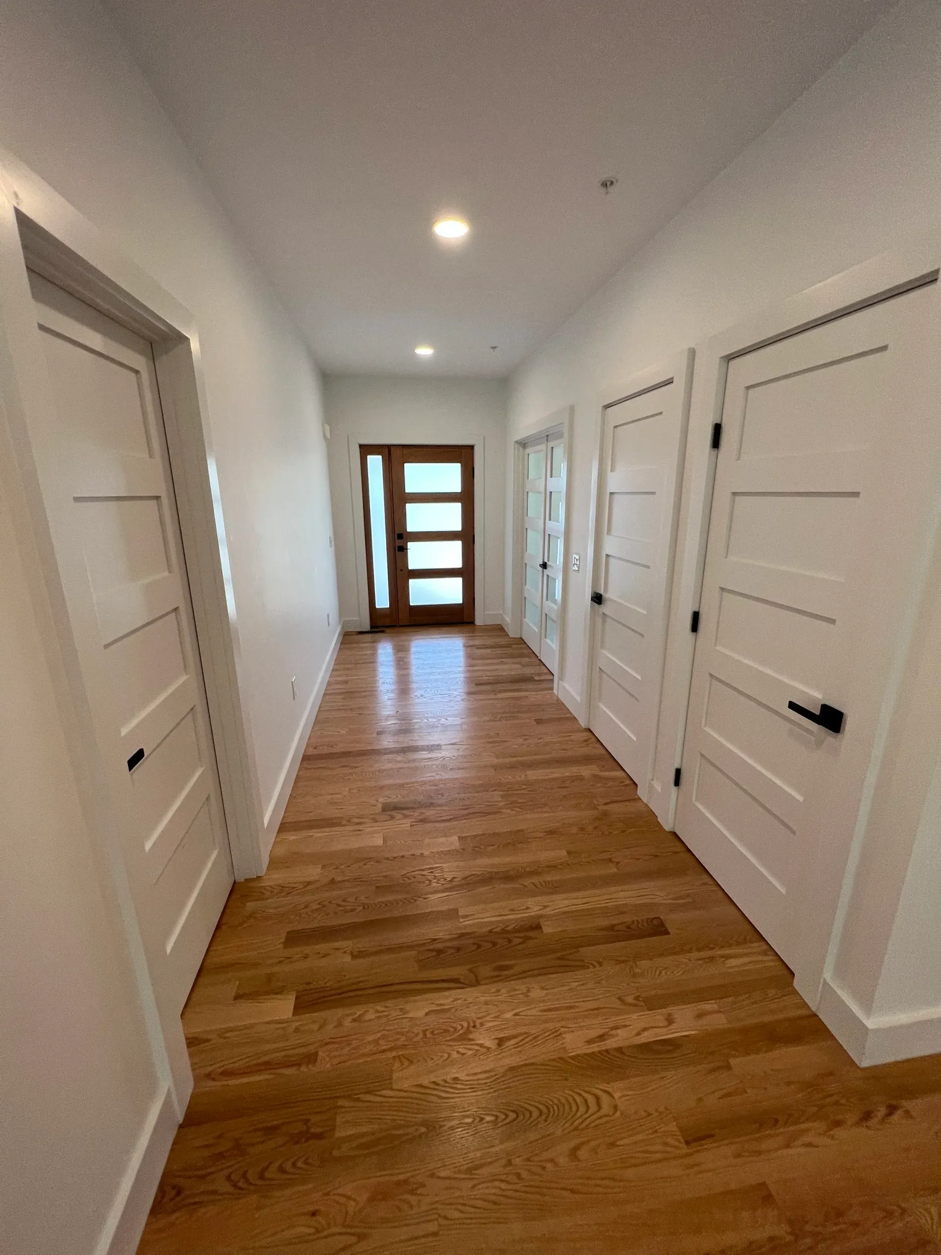 Hallway with wooden floor, white walls and doors. Interior door at the end has glass panes.