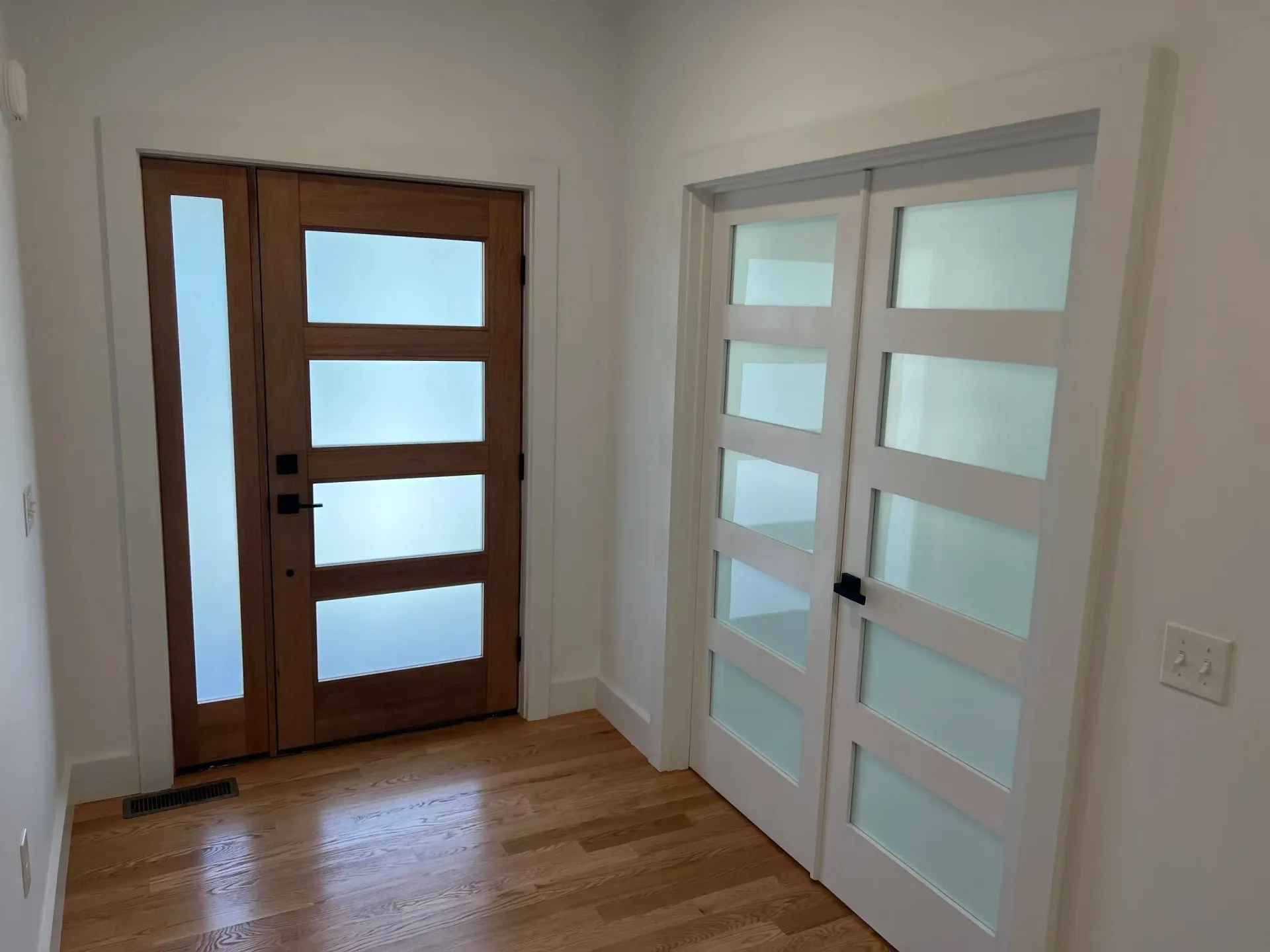 Wooden front door with glass panels and a white door with glass panels.