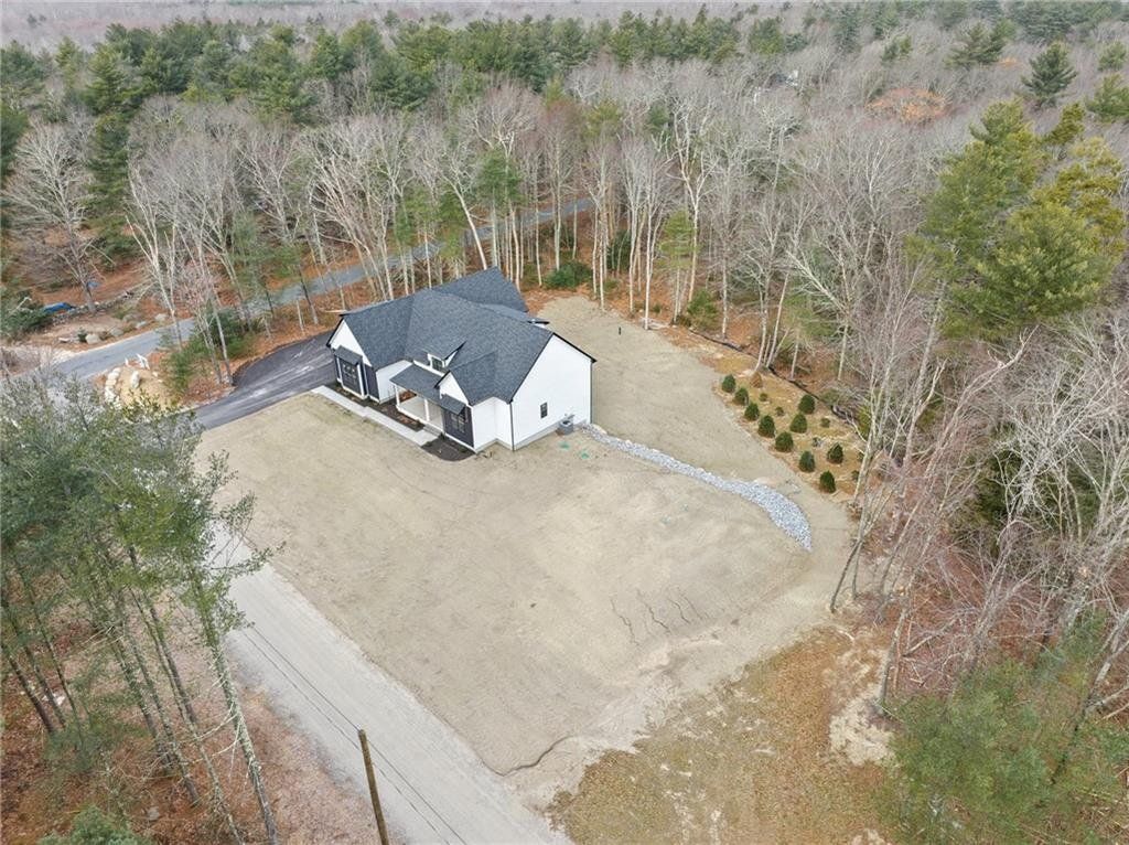 Aerial view of a white house with black roof, surrounded by brown yard and bare trees.