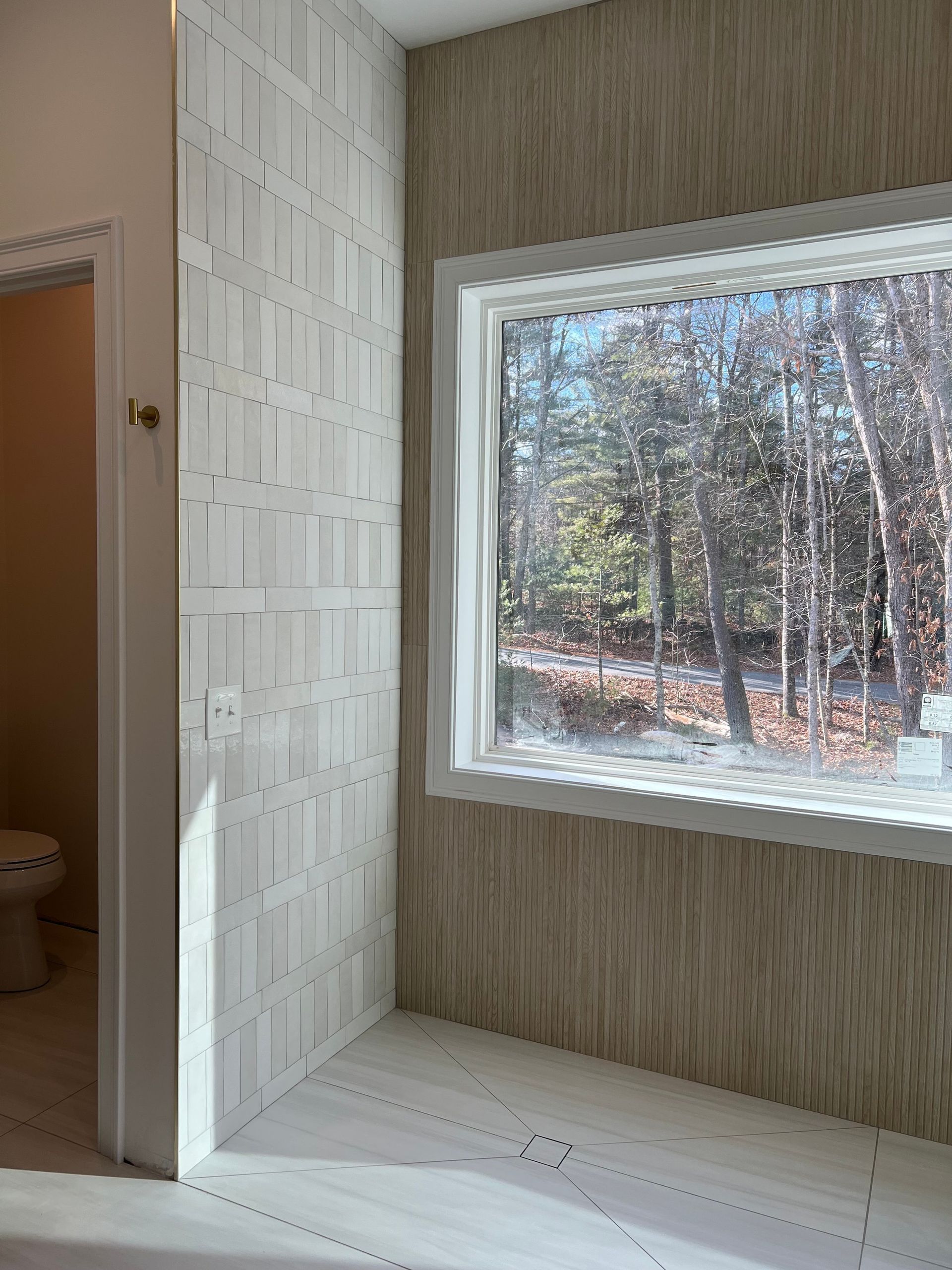 Corner of a room with textured white and tan walls, a window overlooking trees, and an open doorway.