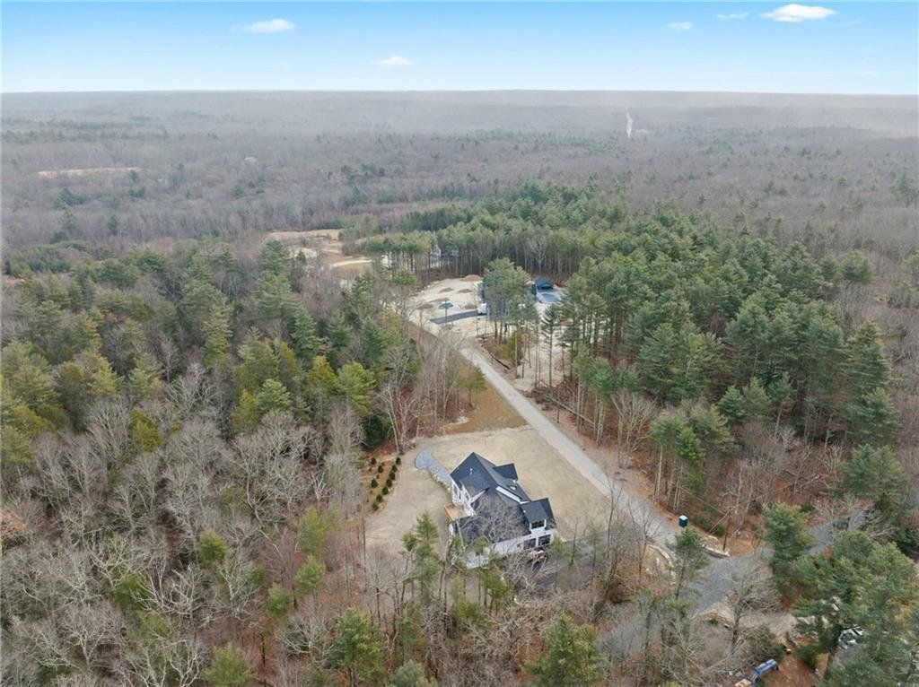 Aerial view of a large house with a dark roof on a wooded property.