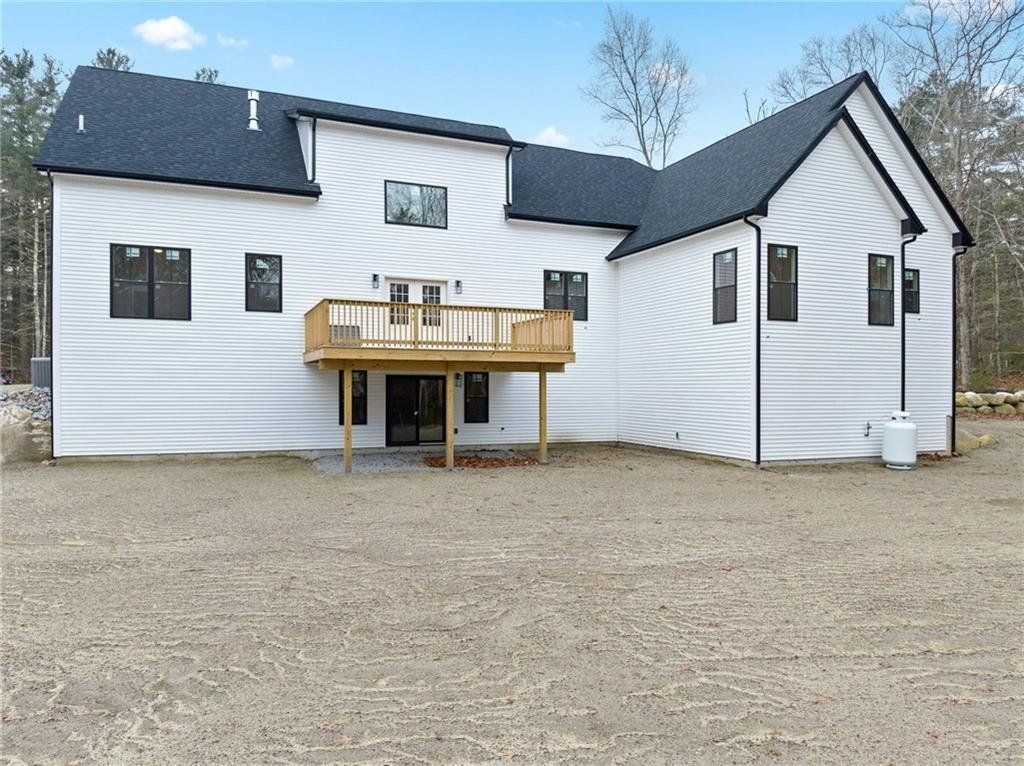 Rear view of a white modern two-story house with a wooden deck and black trim against a cloudy sky.