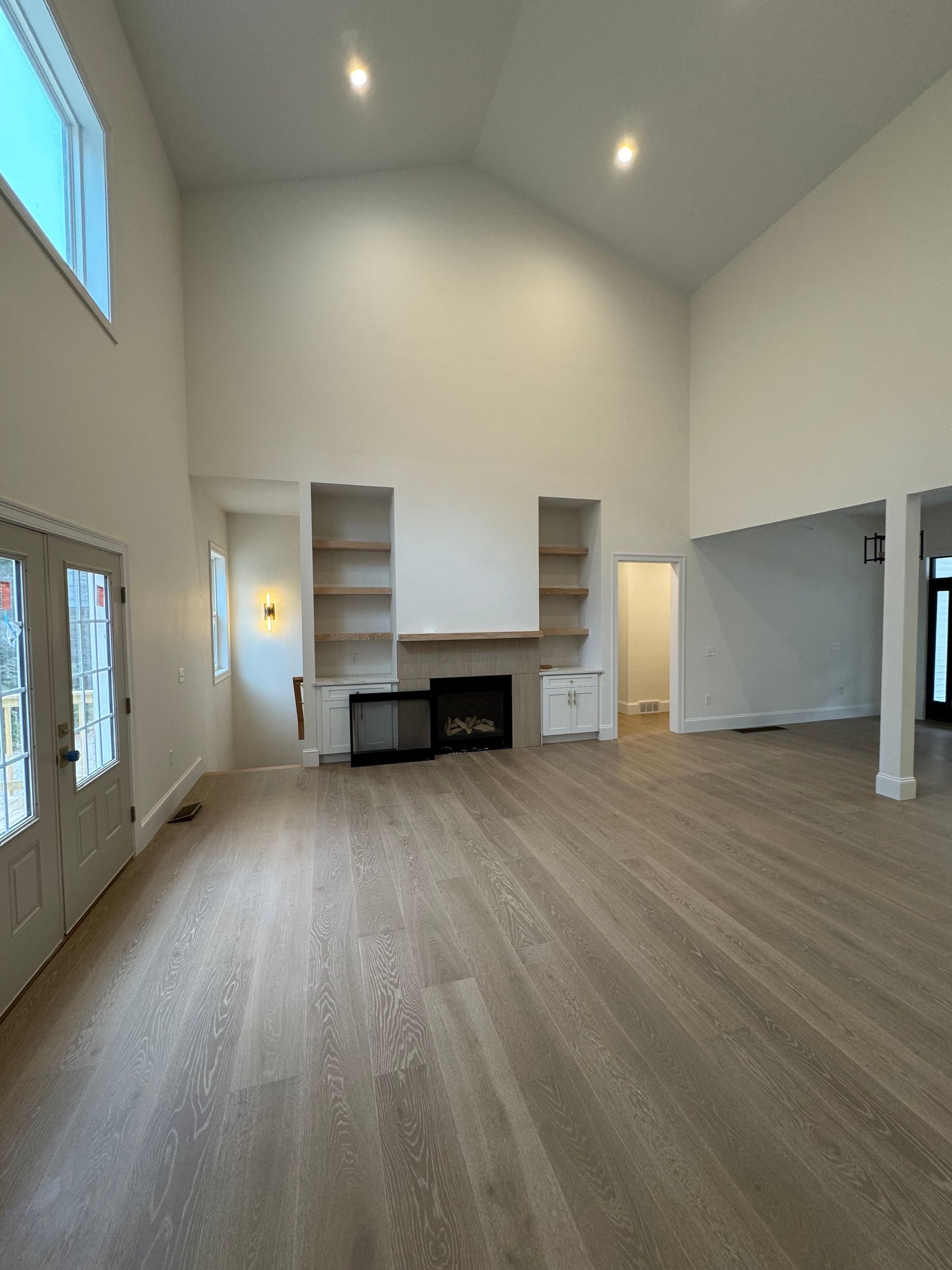 Spacious living room with high ceilings, fireplace, built-in shelving, and light wood flooring.