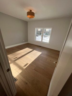 Empty room with light wood floors, window, gray walls, and a decorative light fixture.