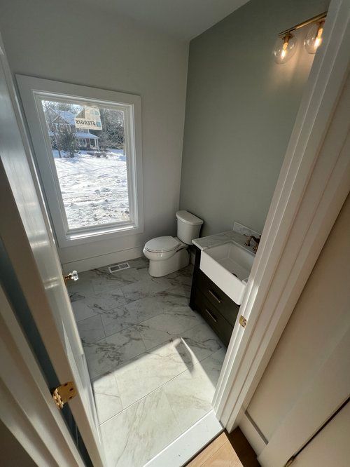 Small bathroom with a toilet, sink, and window; gray and white tile floor.