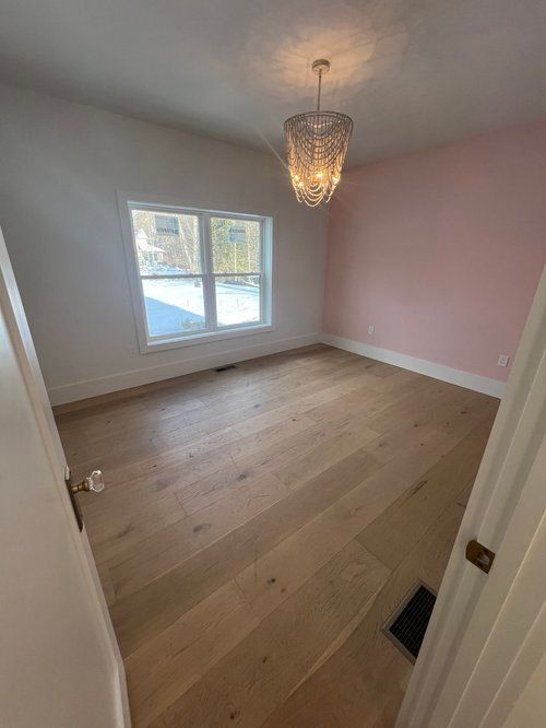 Empty room with light wood floors, a pink wall, and a crystal chandelier.